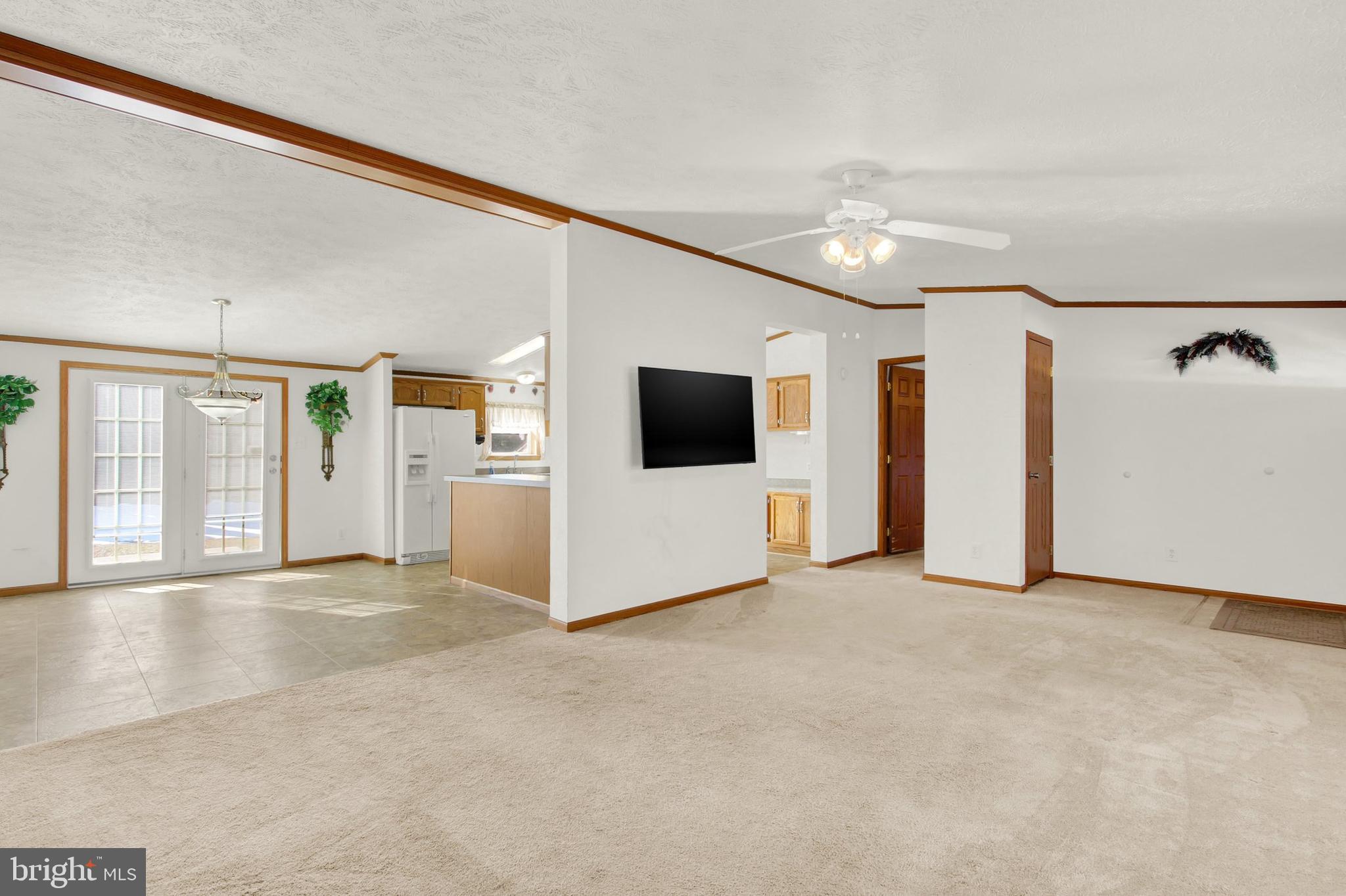 Open-plan living room and kitchen with beige carpet, tile flooring, and French patio doors.