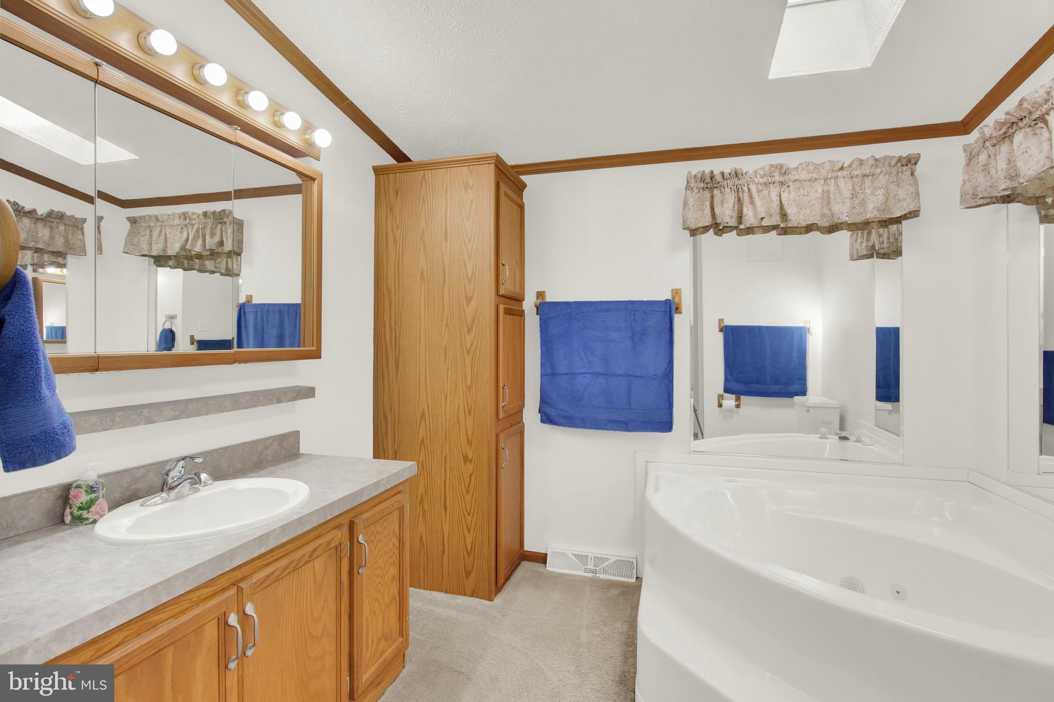 Bathroom with a large soaking tub, mirrored walls, and oak vanity cabinetry.