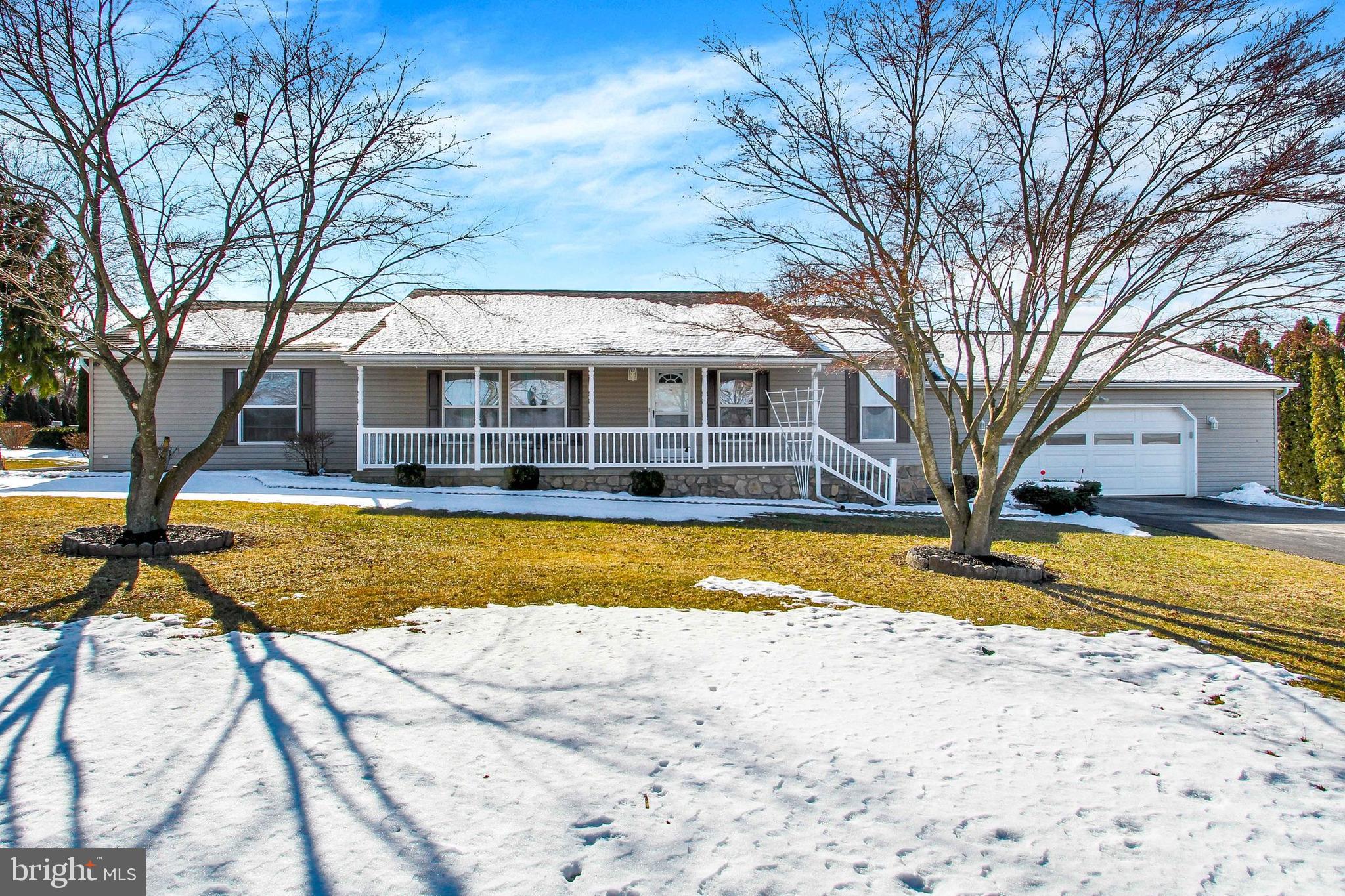 Gray single-story home with a long front porch and attached garage, framed by bare trees and patches of snow.