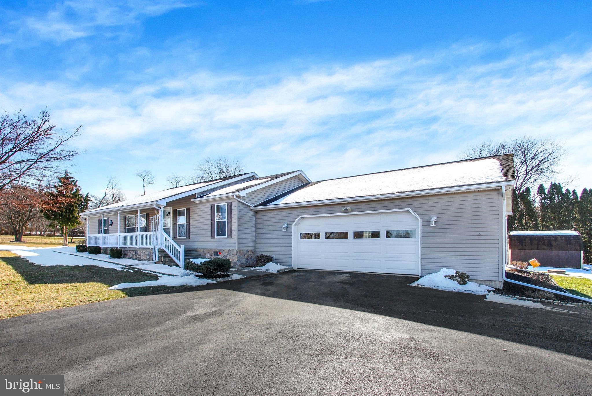 Gray single-story home with a covered porch, attached garage, and snow on the roof.