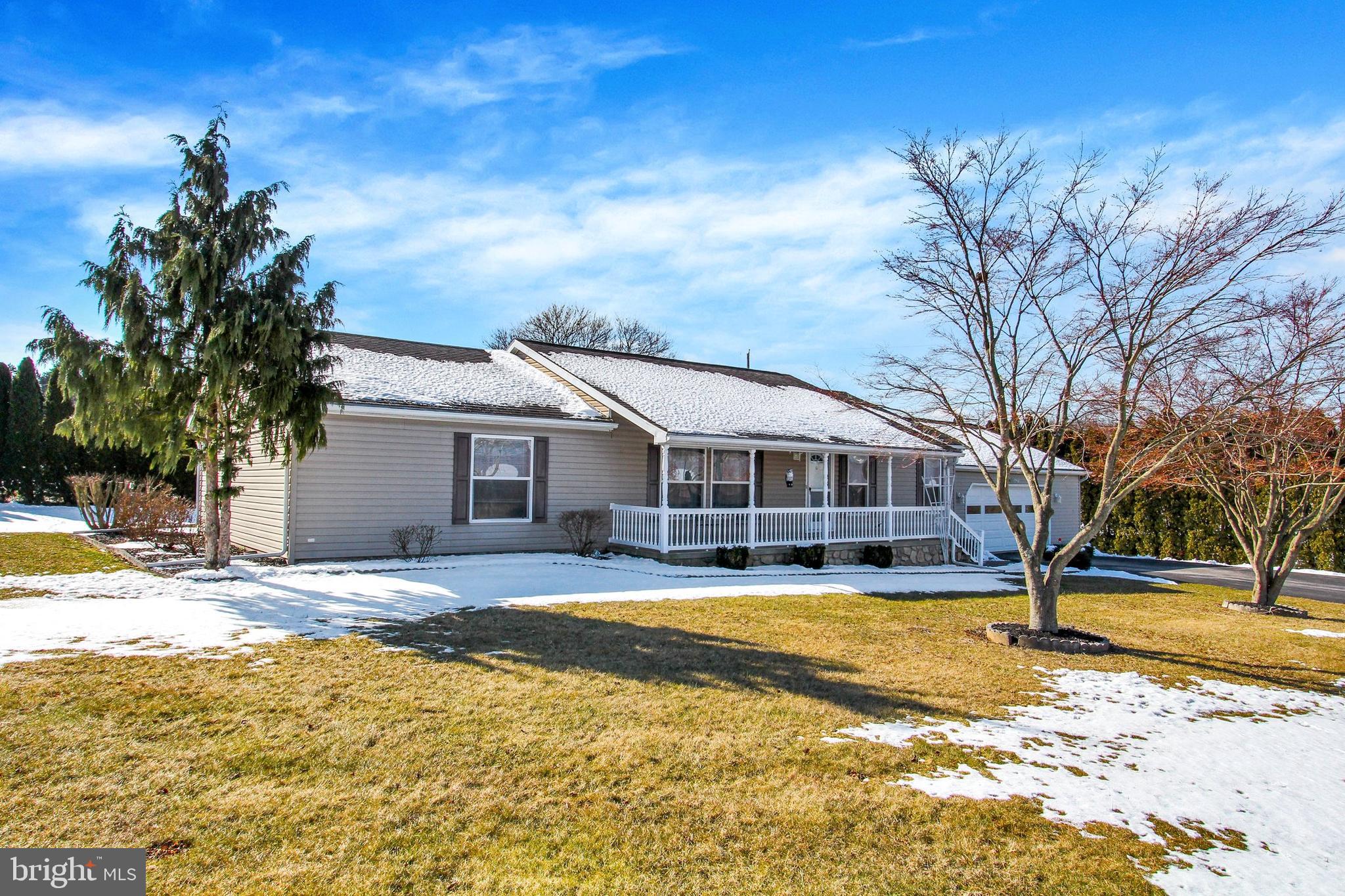 Gray ranch house with a white-railed porch and attached garage, surrounded by patchy snow.