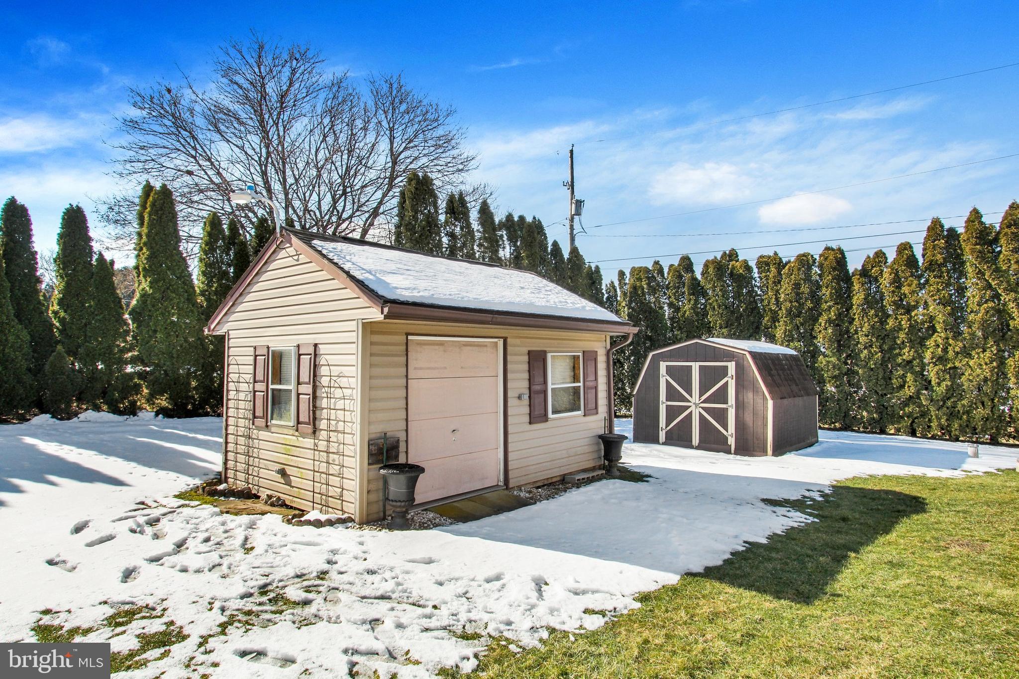 Beige detached garage and dark storage shed in a snow-covered yard.