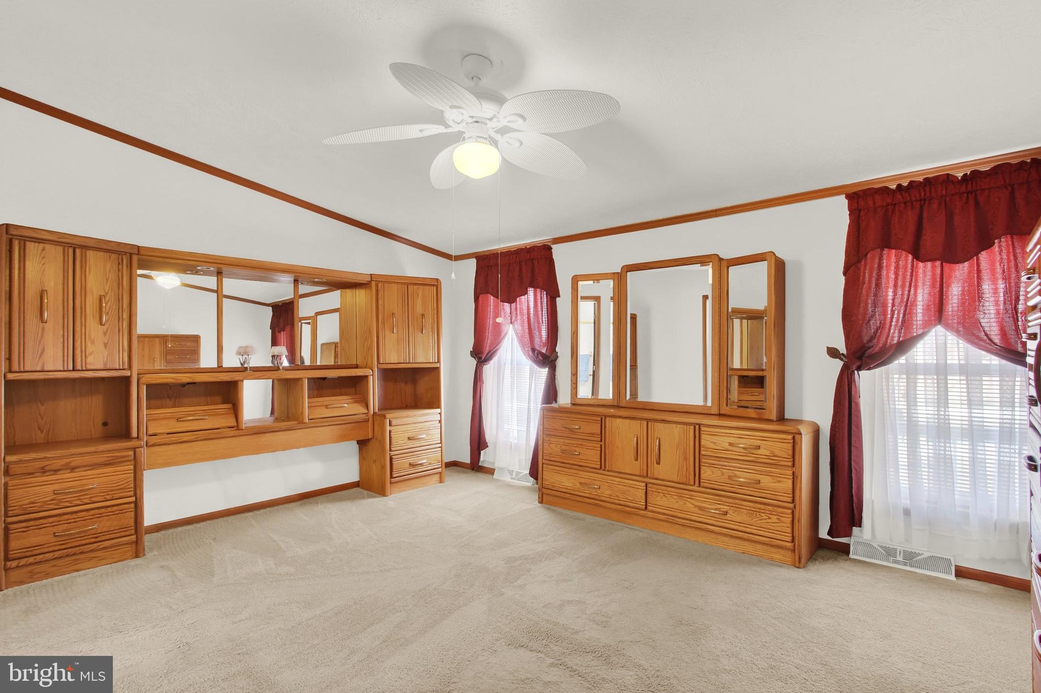 Bedroom with extensive honey-colored built-in wardrobes, matching mirrored dresser, and burgundy curtains.