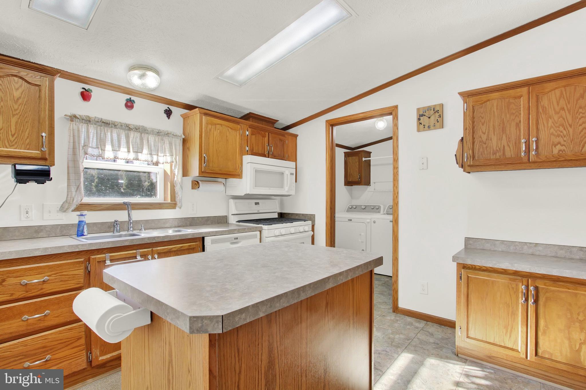 Kitchen with oak cabinets, a large countertop peninsula, white appliances, and laundry area through the doorway.