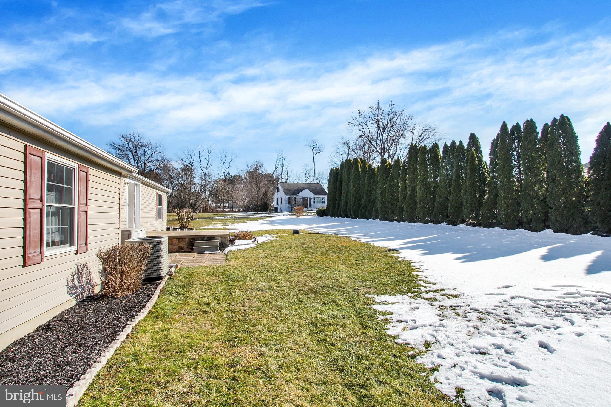 Backyard with a patio, snow-dusted lawn, and tall evergreen hedge beside the house.
