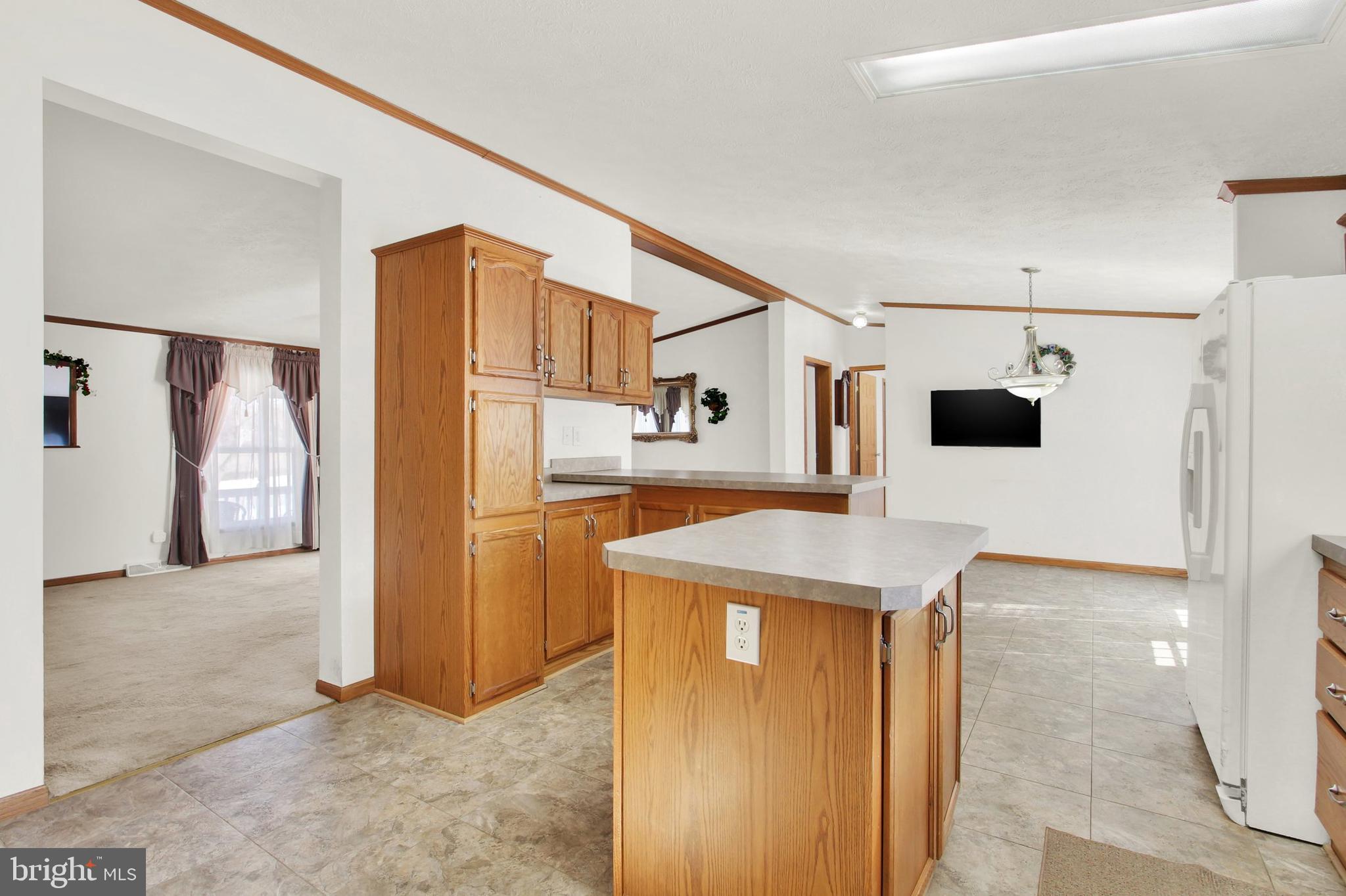 Kitchen with wood cabinetry, a central island, tiled floors, and an adjoining carpeted dining area.