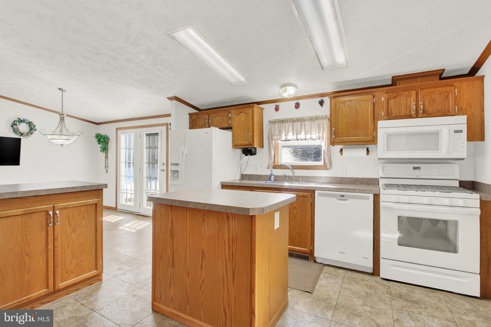 Kitchen with wood cabinets, a central island, white appliances, and glass doors.