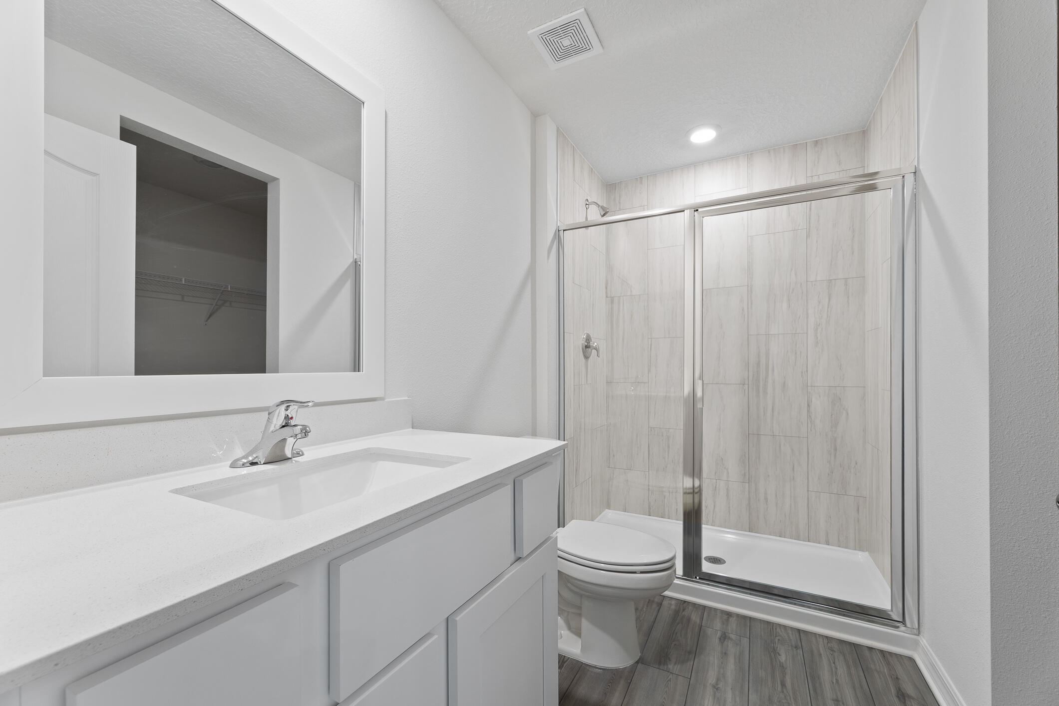 Bathroom with a wide vanity, framed mirror, toilet, and glass-enclosed tiled shower.