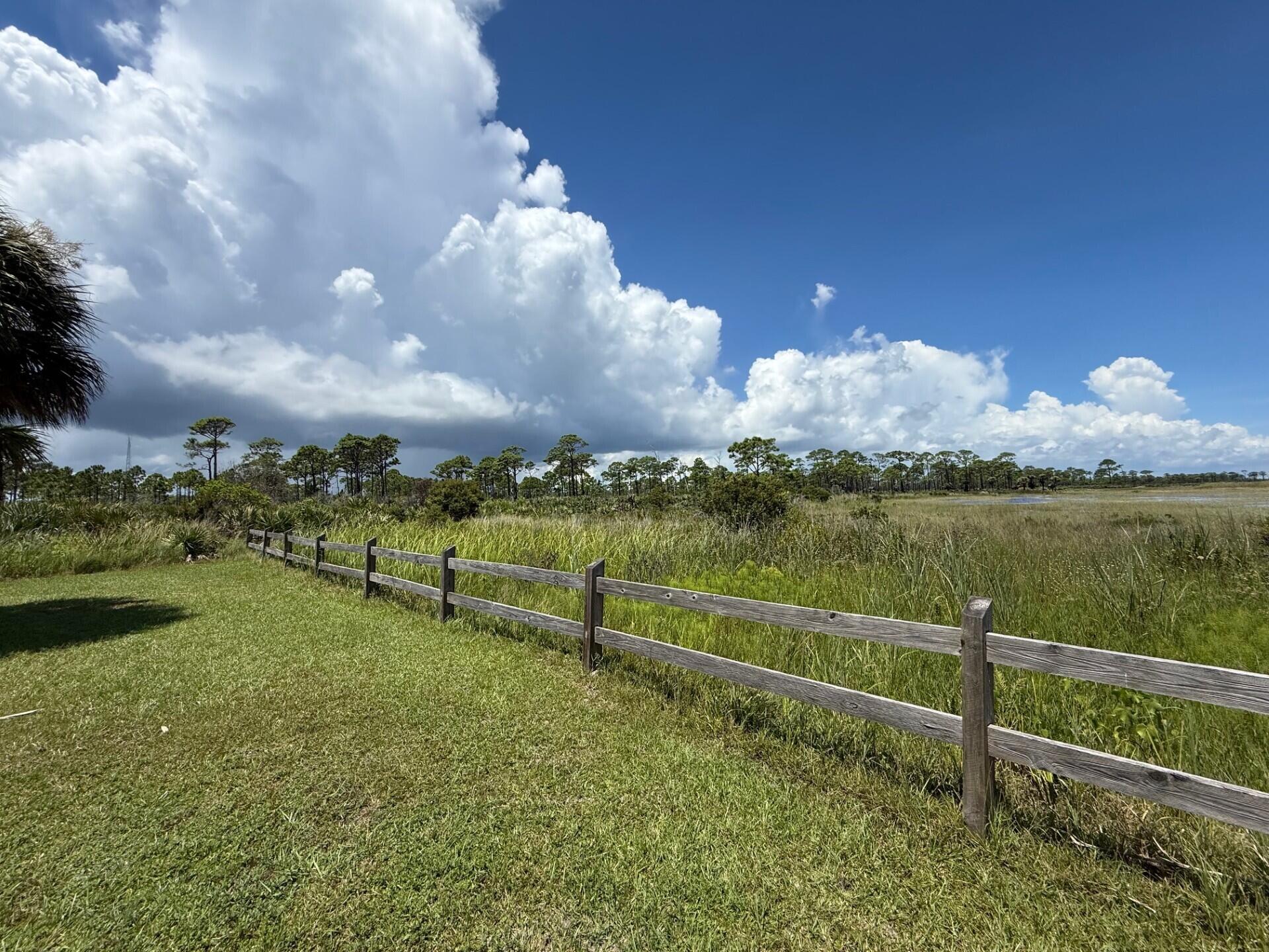 Grassy yard bordered by a wooden fence overlooking marshland and a distant tree line.
