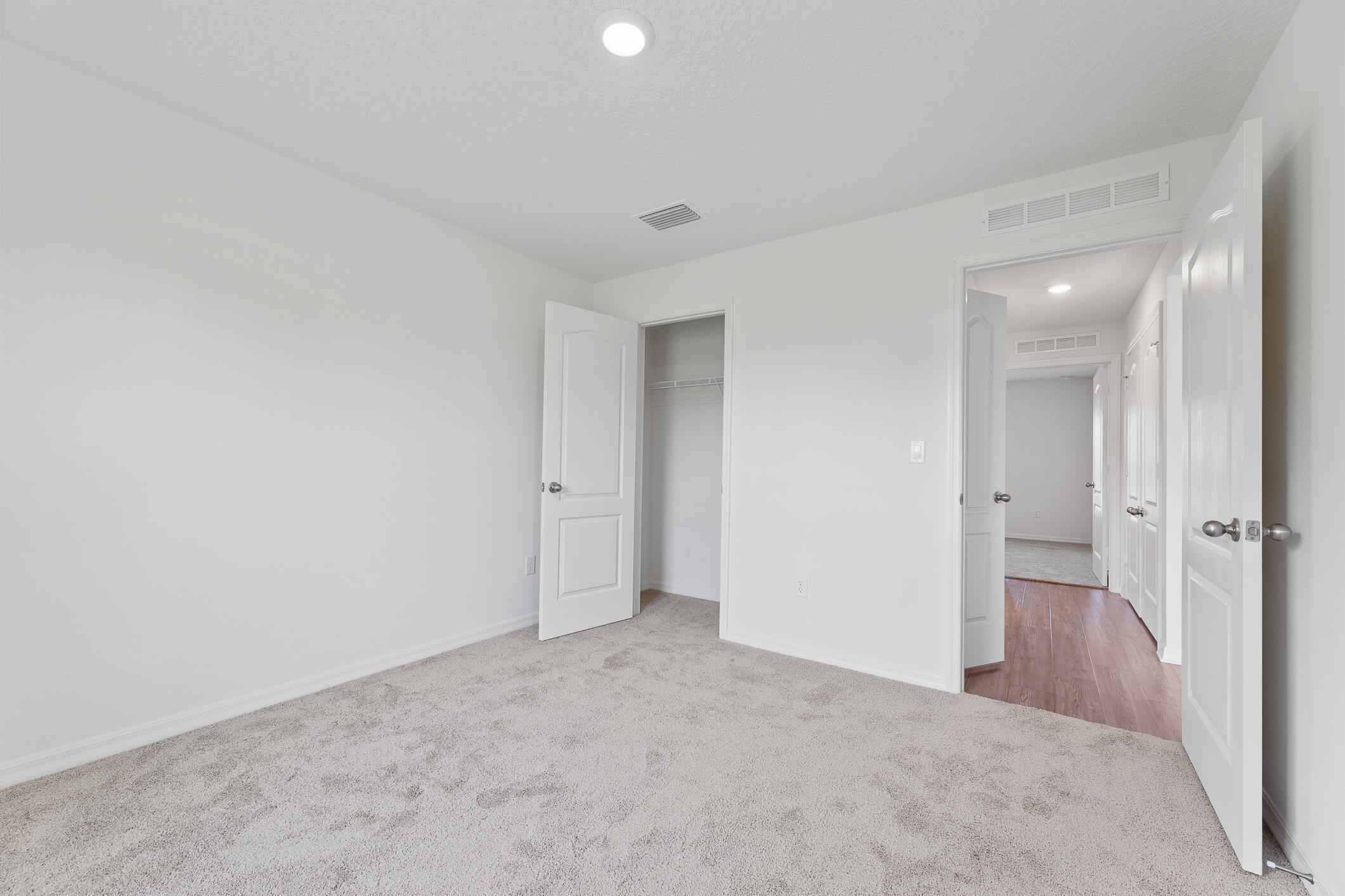 Unfurnished carpeted bedroom with an open closet and doors leading to the hallway.