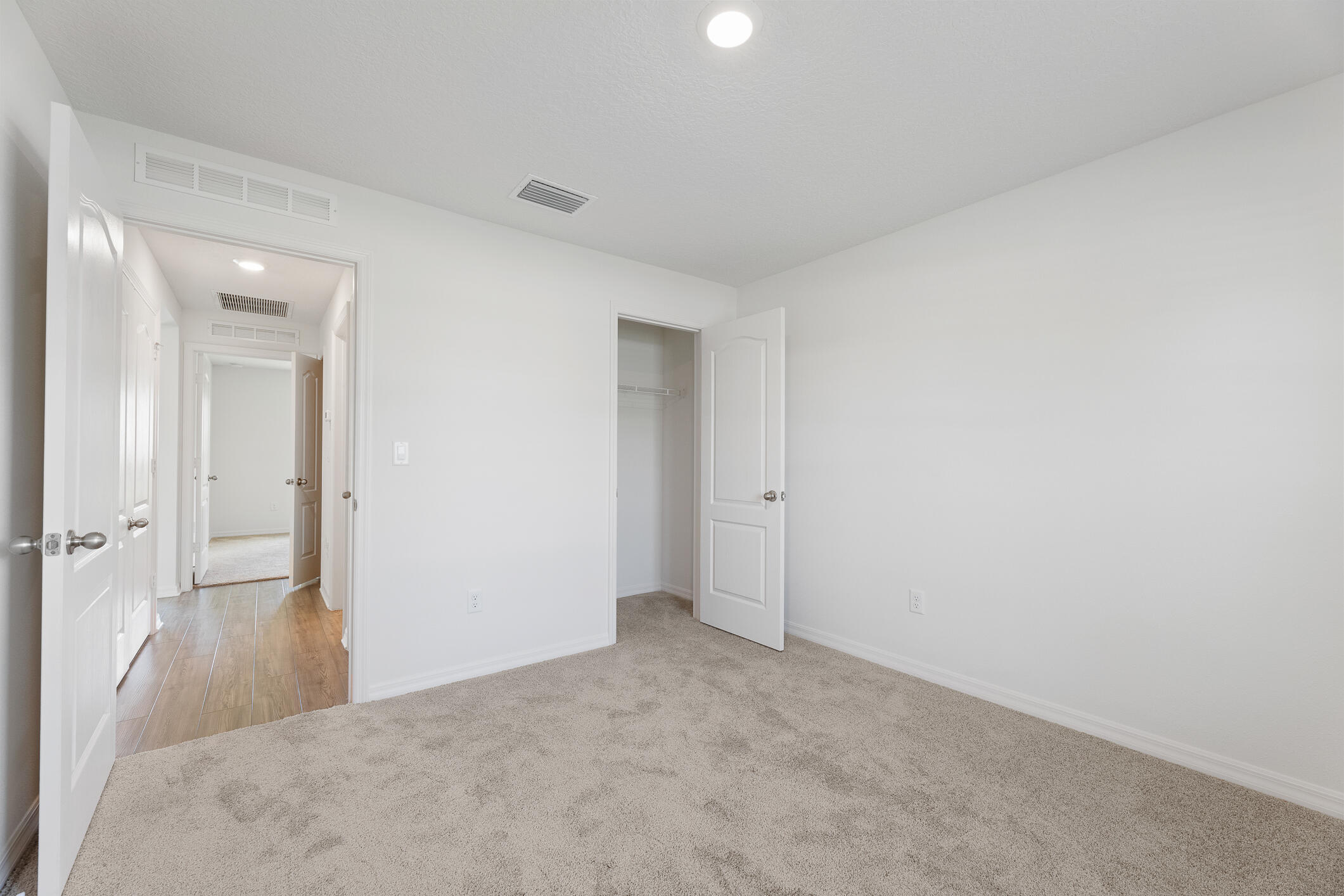 Empty carpeted bedroom with an open closet and a hallway visible through the doorway.