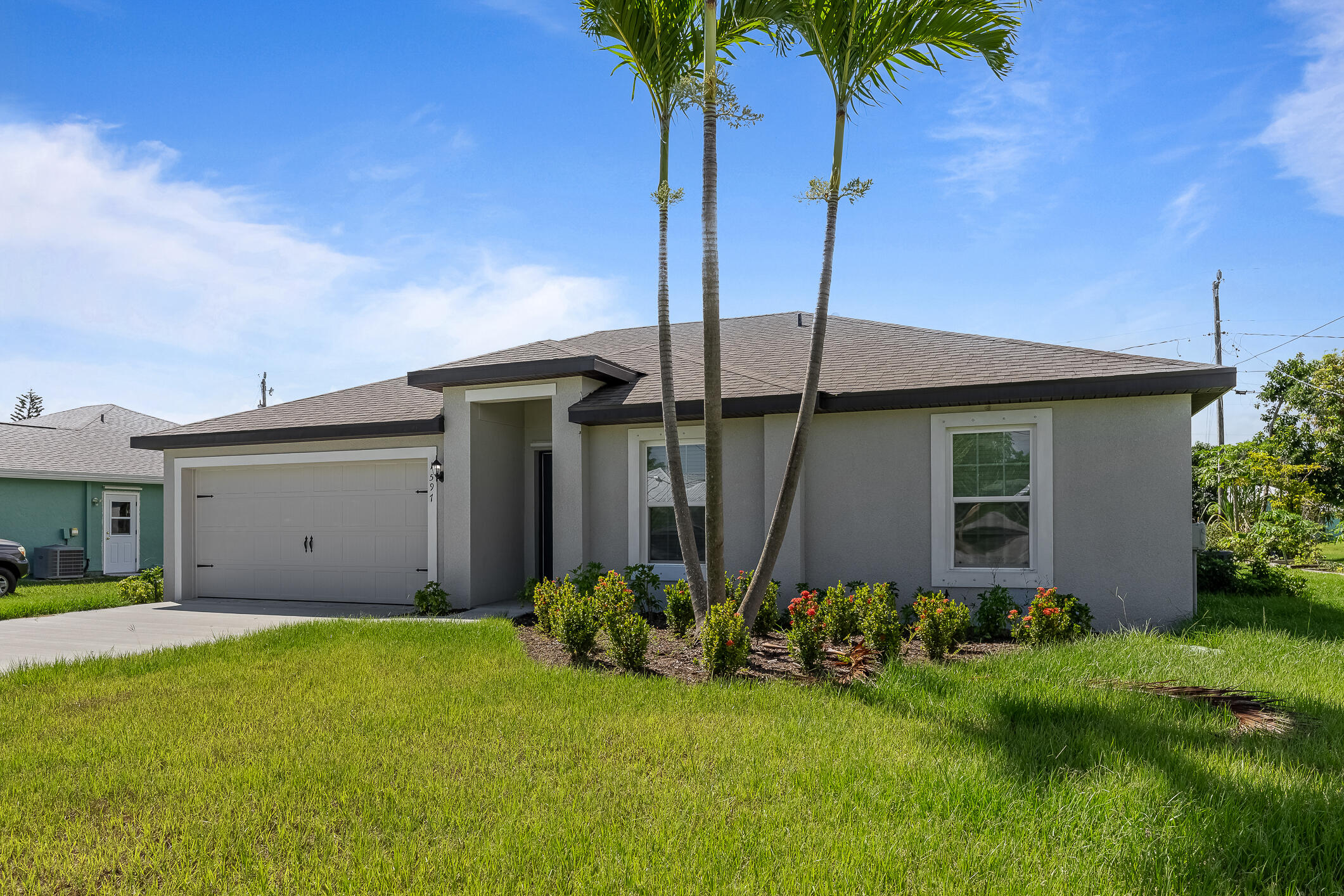 Single-story home with a two-car garage, palm trees, and landscaped front lawn.