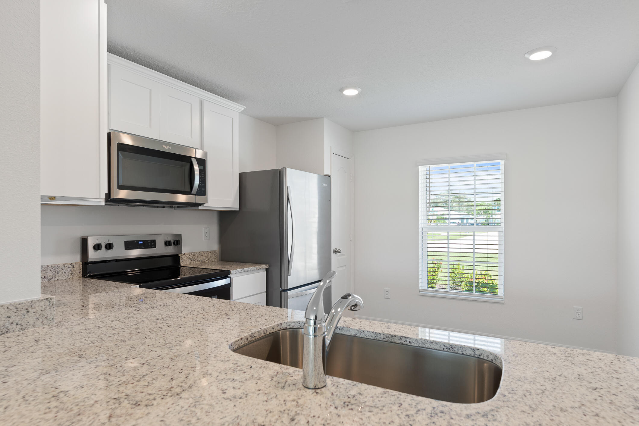 Kitchen with granite breakfast bar, double sink, white cabinets, and stainless steel appliances.