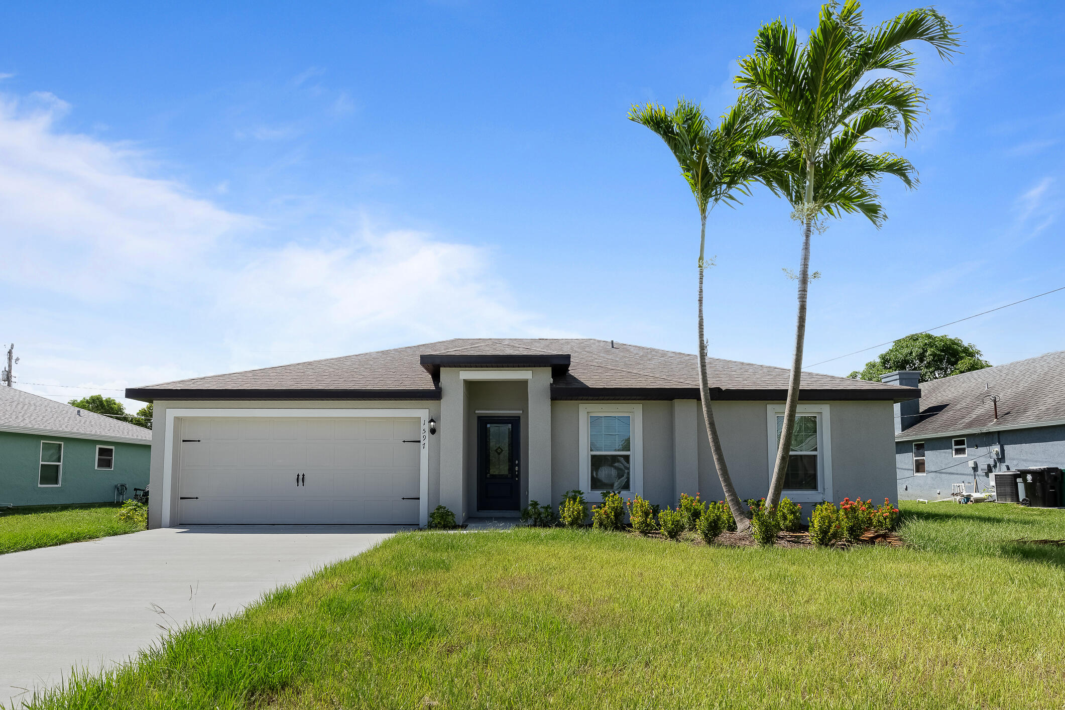 Gray single-story home with a two-car garage, front lawn, and tall palm trees.