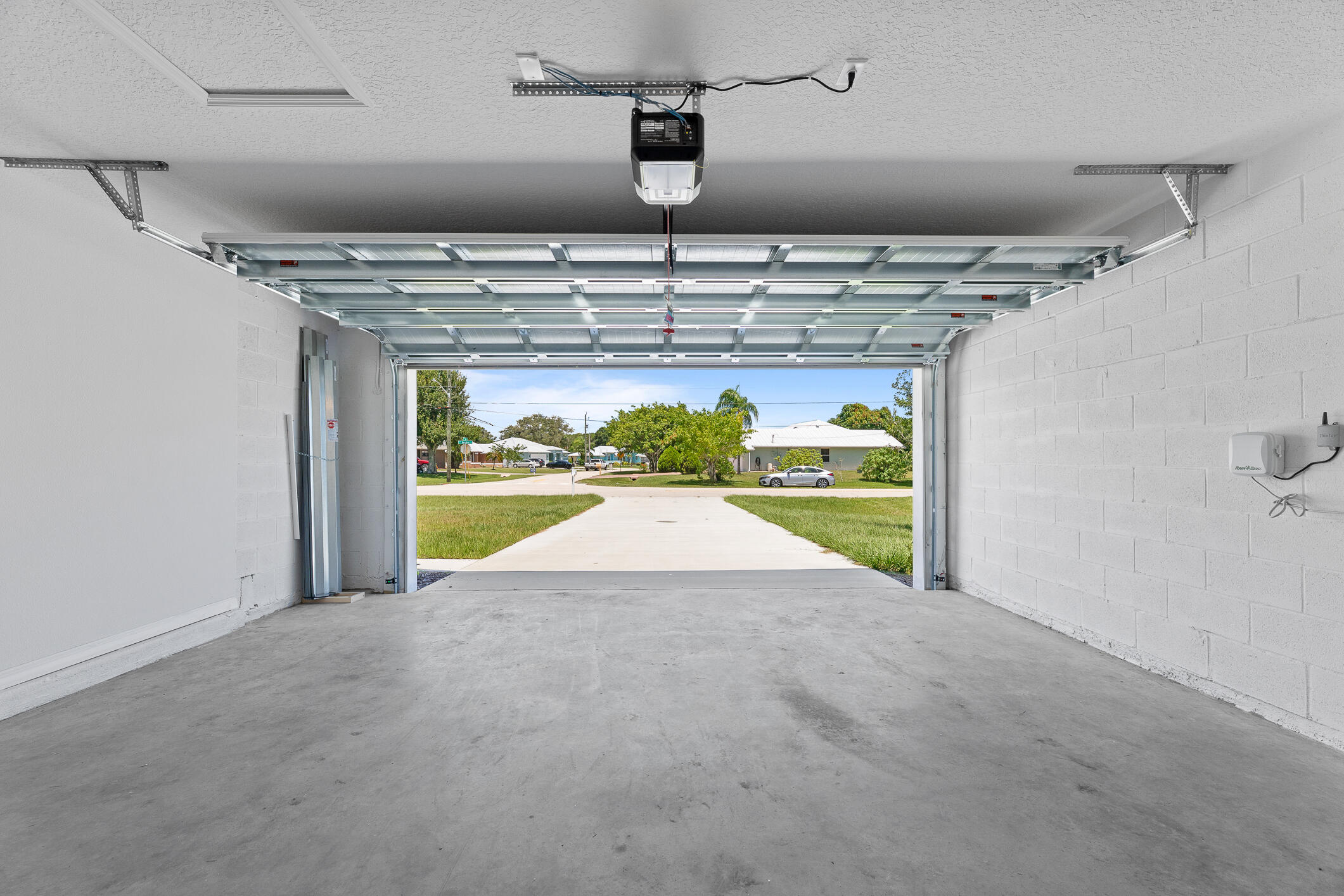 Empty garage with its overhead door open to a sunny driveway and residential street.