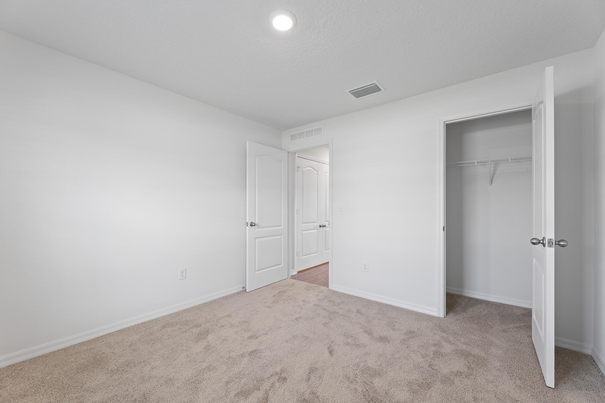 Empty carpeted bedroom with an open closet and white doors.