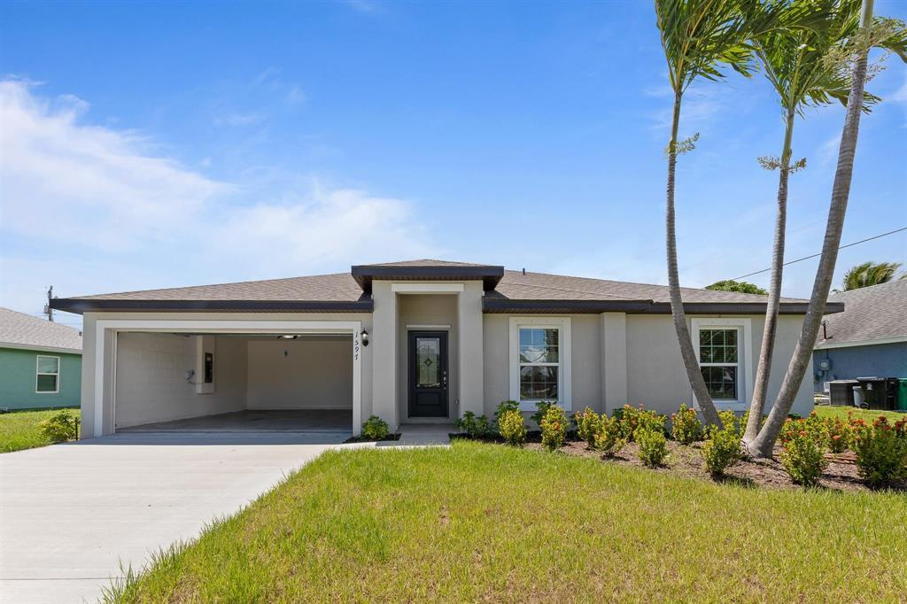 Single-story gray home with an attached garage, palm trees, and a broad concrete driveway.