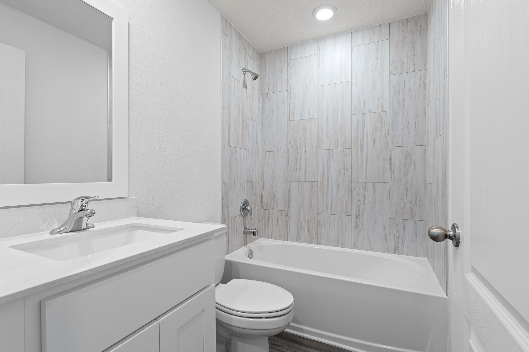 Bathroom with a white vanity, toilet, and bathtub surrounded by large gray wood-look tiles.