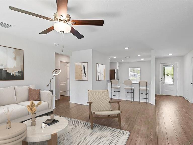 Open-plan living and dining area with a ceiling fan, breakfast bar, and wood-look flooring.