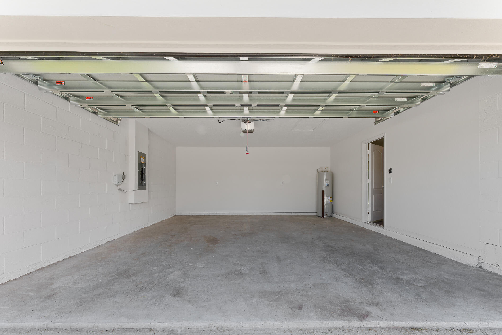 Empty two-car garage with a raised segmented door, concrete floor, and water heater.
