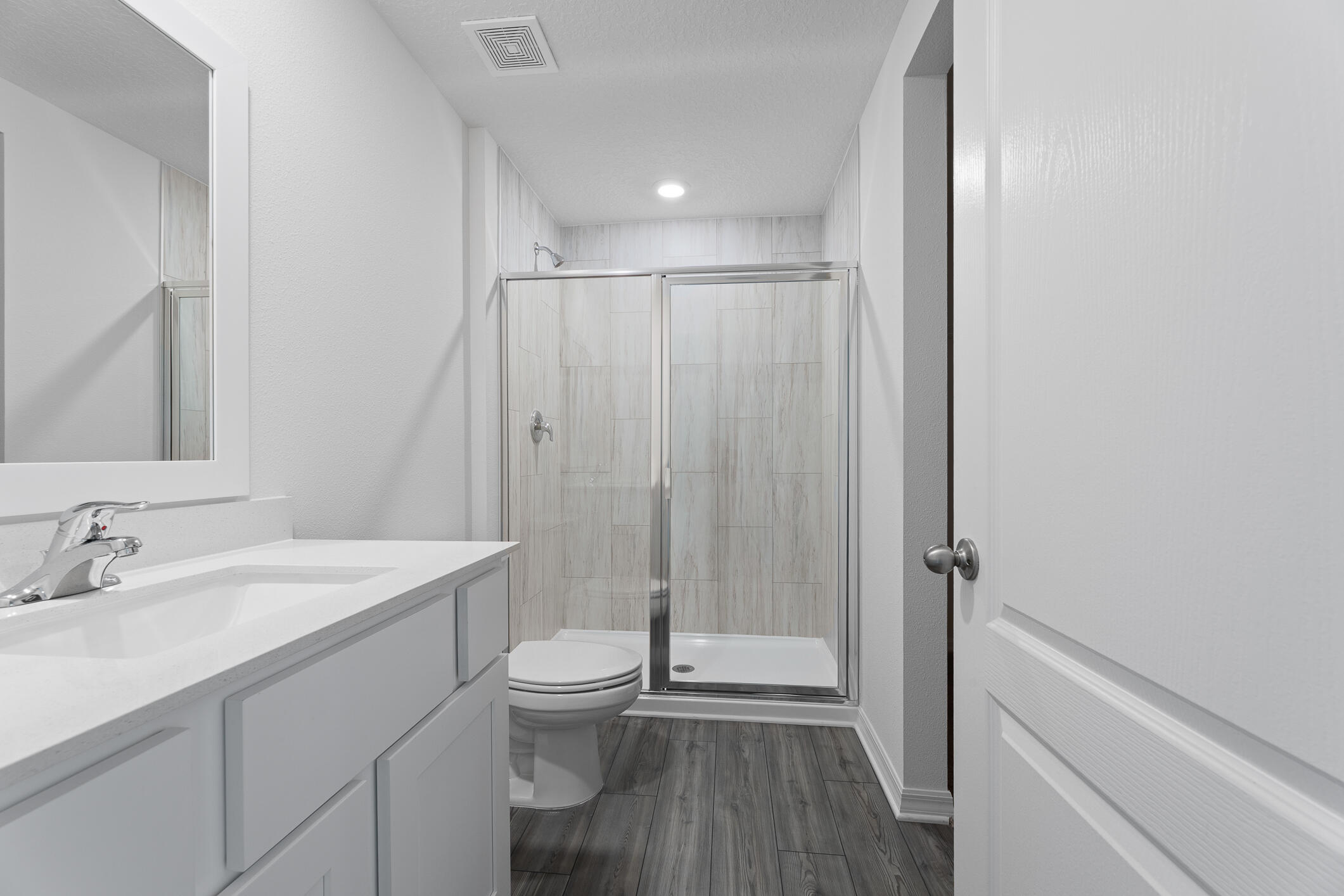 Bathroom with a glass-enclosed tiled shower, white vanity, and dark wood-look flooring.
