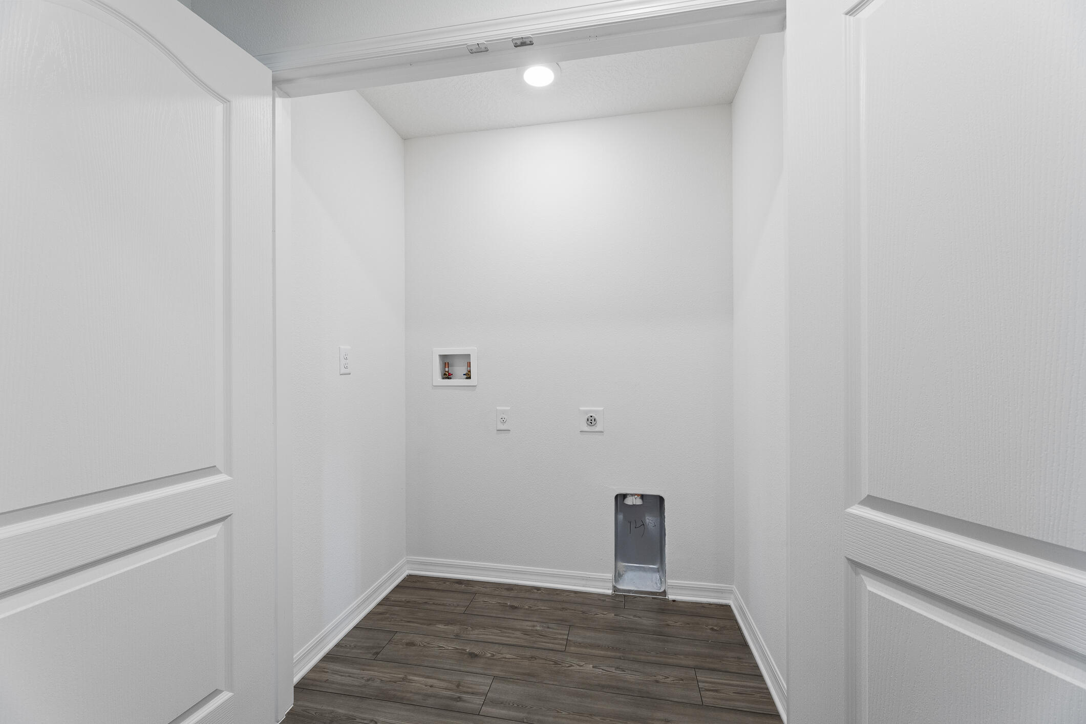 Empty laundry closet with washer and dryer hookups and dark wood-look flooring.