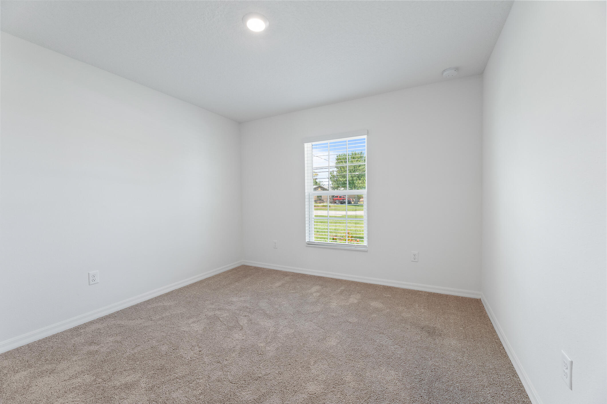 Empty bedroom with beige carpet, white walls, and a window with blinds.