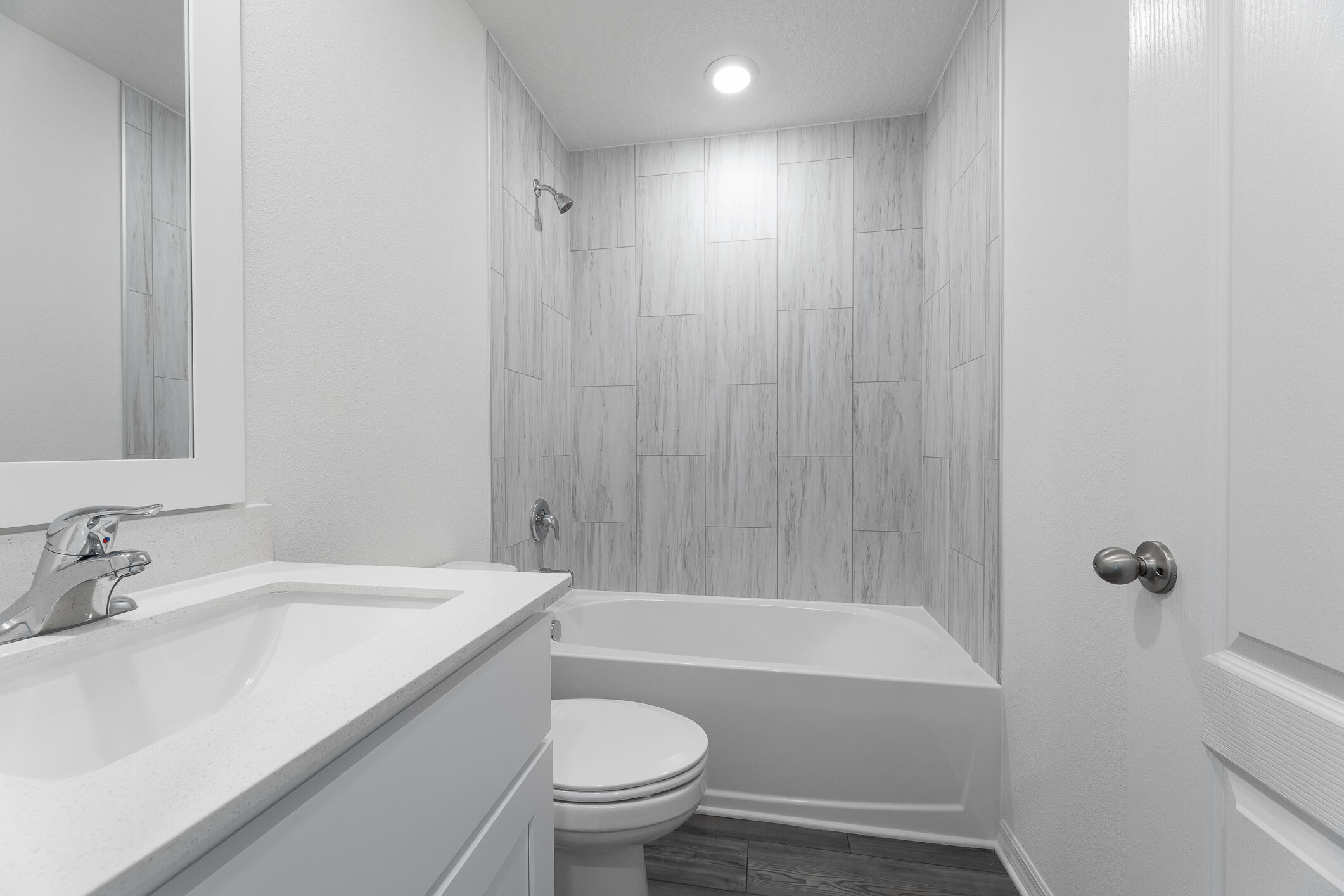 Bathroom with a white vanity, toilet, and tub-shower lined with gray tile.