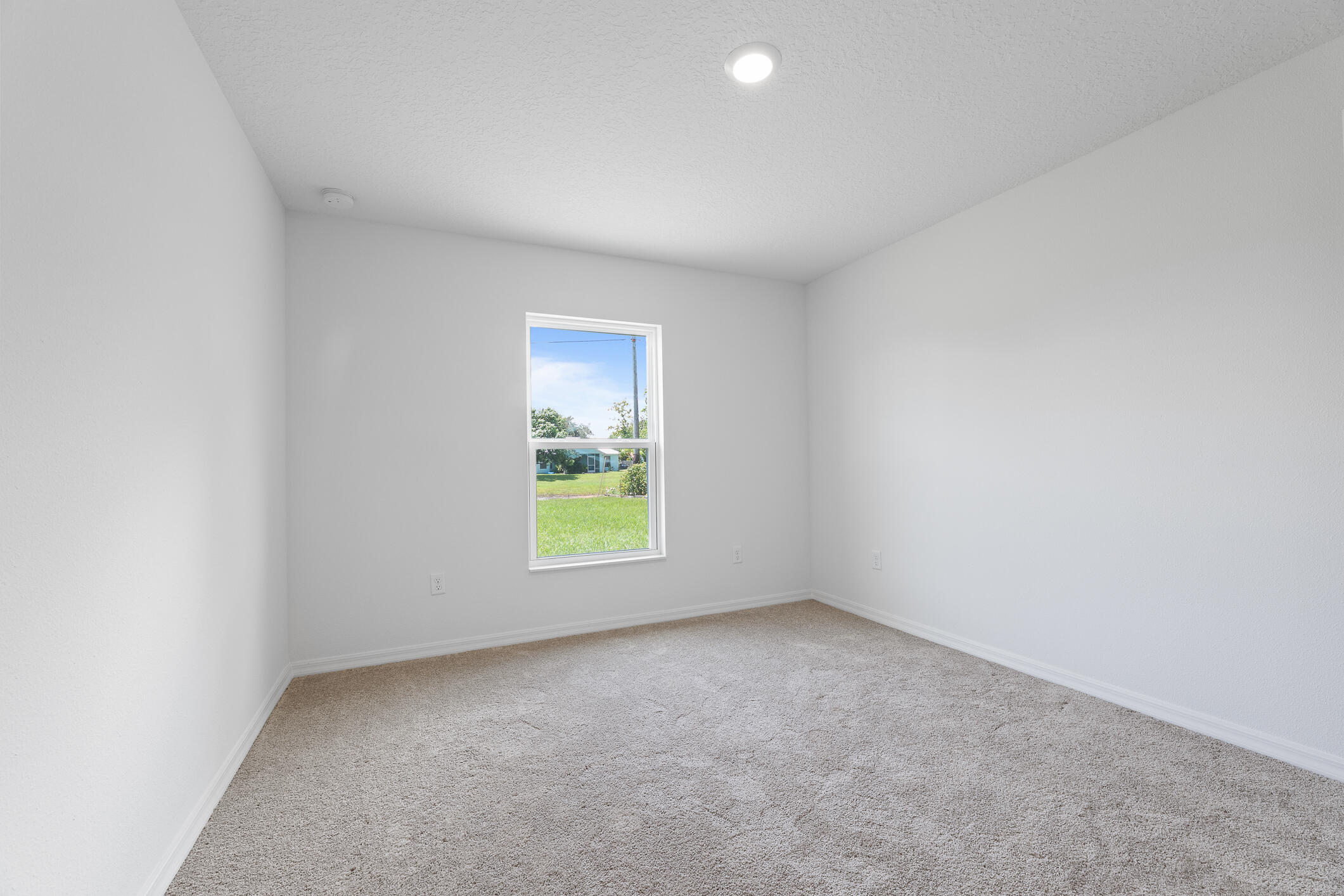 Empty carpeted room with white walls and a single window overlooking a lawn.