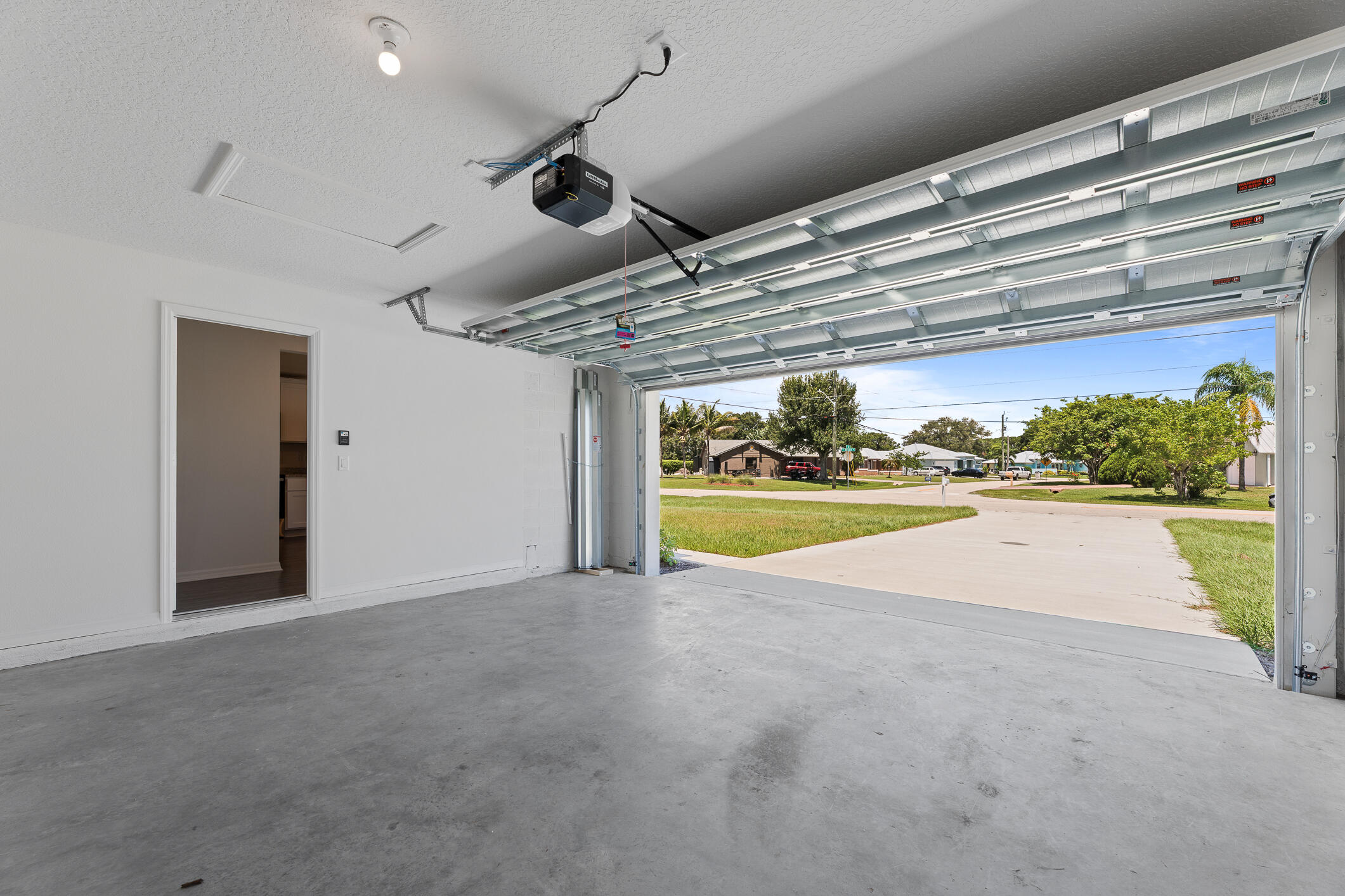 Empty garage with its overhead door open to a sunny residential street.