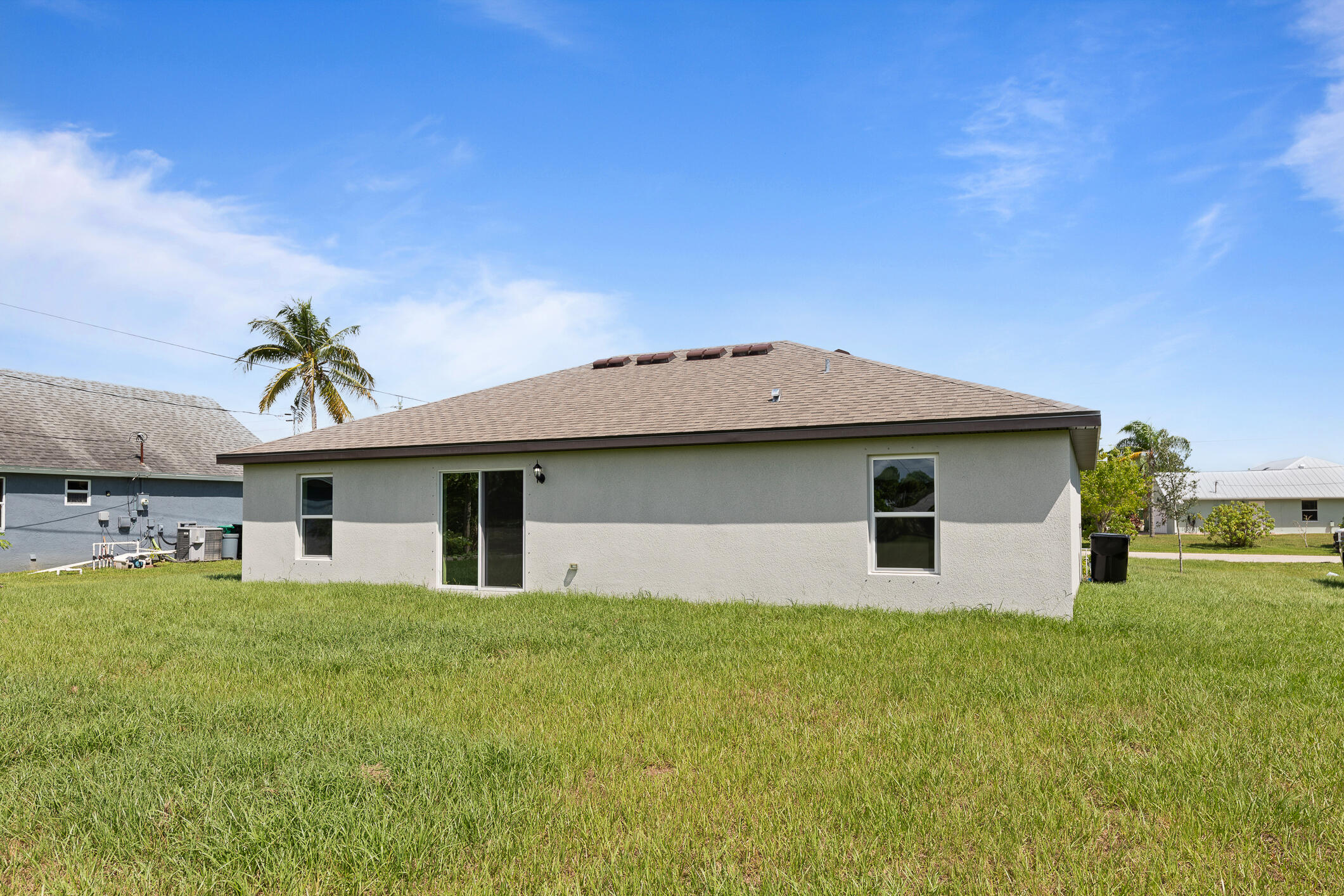 Rear exterior of a single-story stucco home with a broad lawn and sliding glass door.