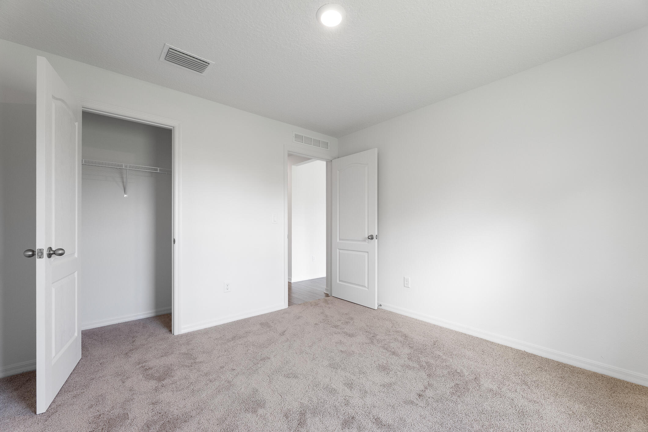 Empty carpeted bedroom with an open closet and two open doors.