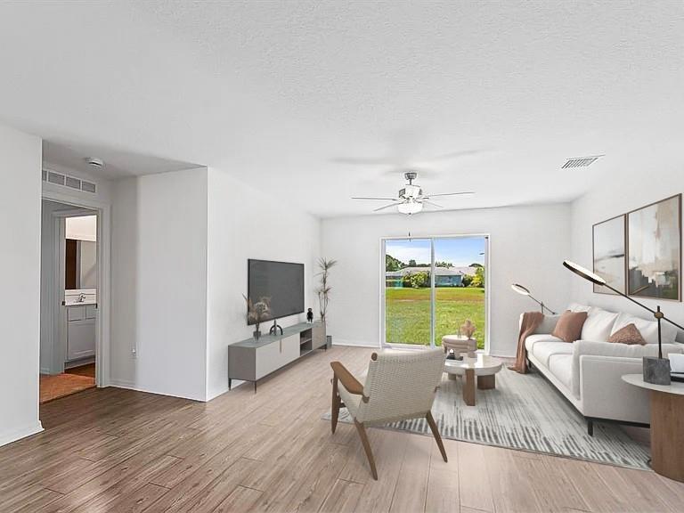 Staged living room with a white sofa, ceiling fan, and sliding glass doors opening to the yard.