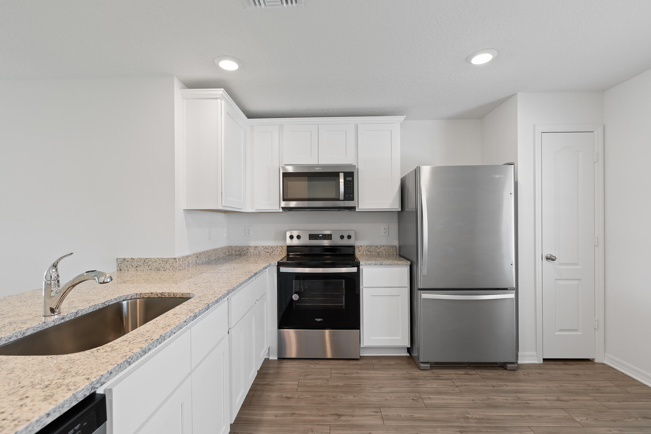 Bright white kitchen with granite counters, stainless steel appliances, and a wide sink.