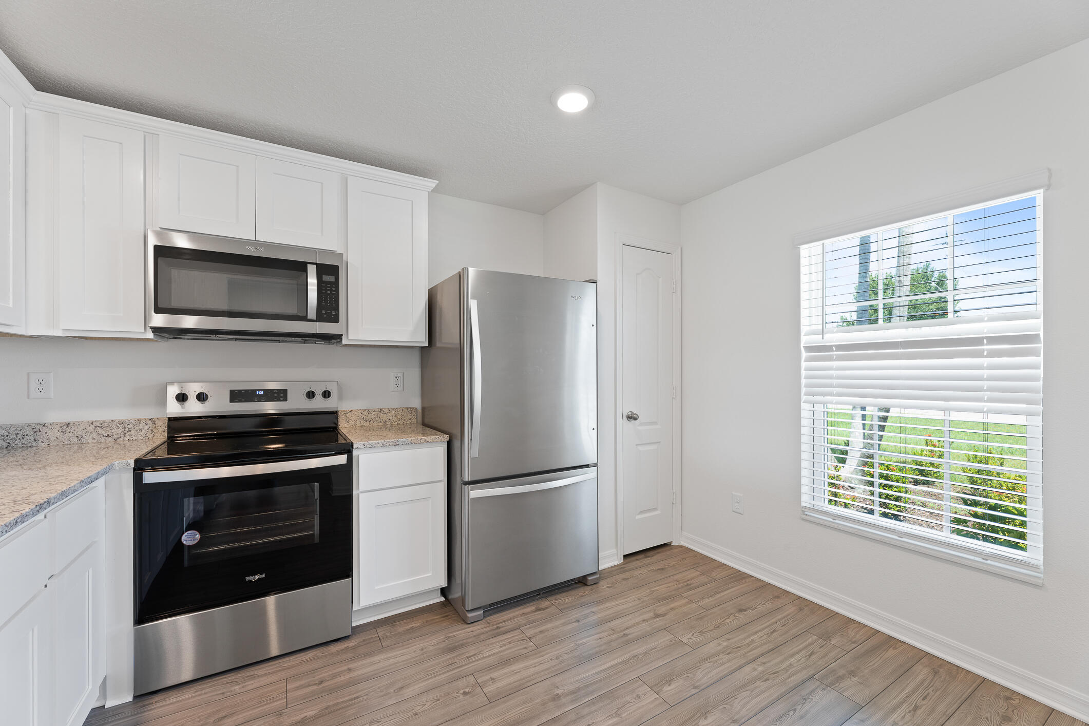 Bright kitchen with white cabinets, stainless steel appliances, granite counters, and wood-look flooring.