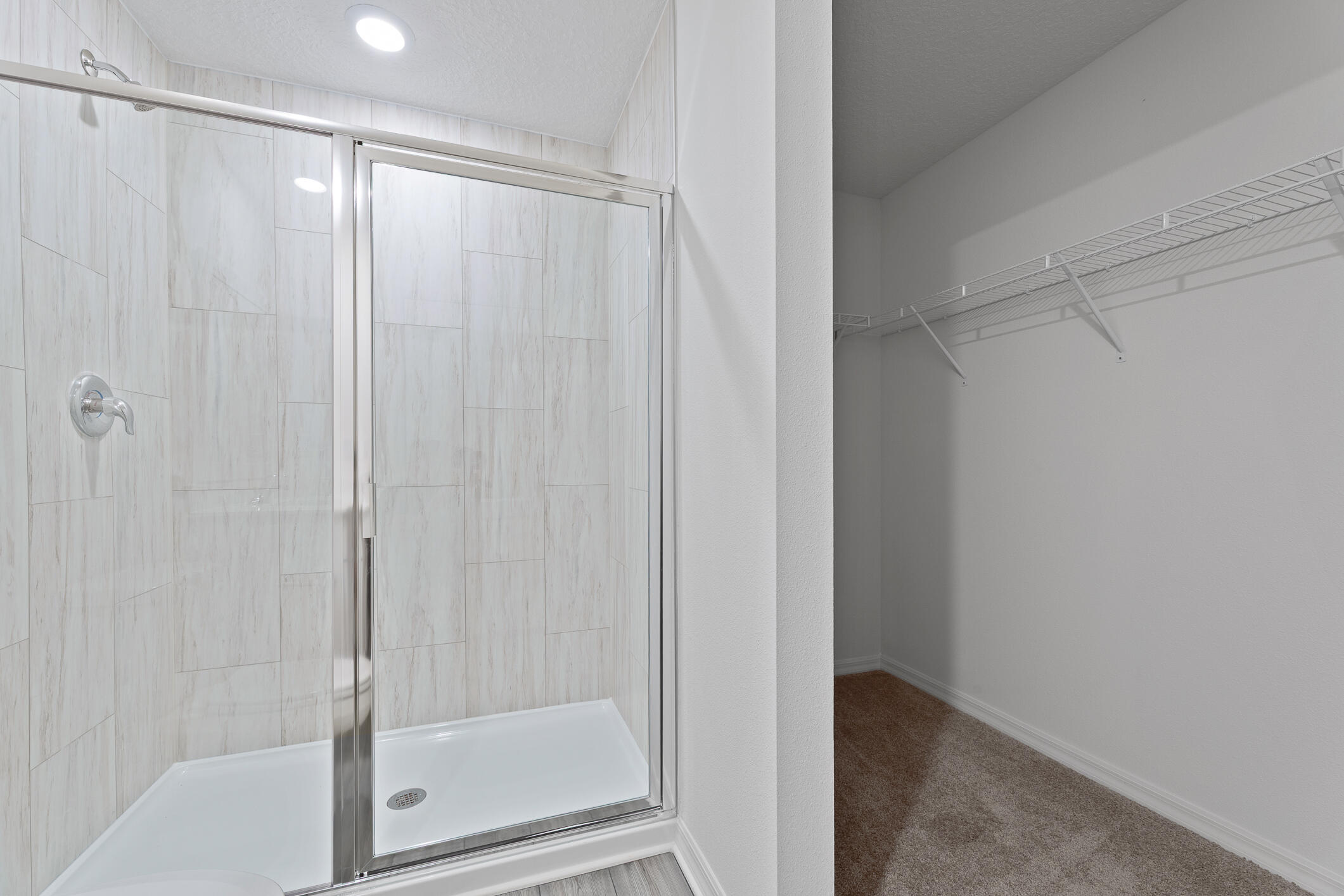 Bathroom with a glass-enclosed tiled shower beside an empty carpeted walk-in closet.
