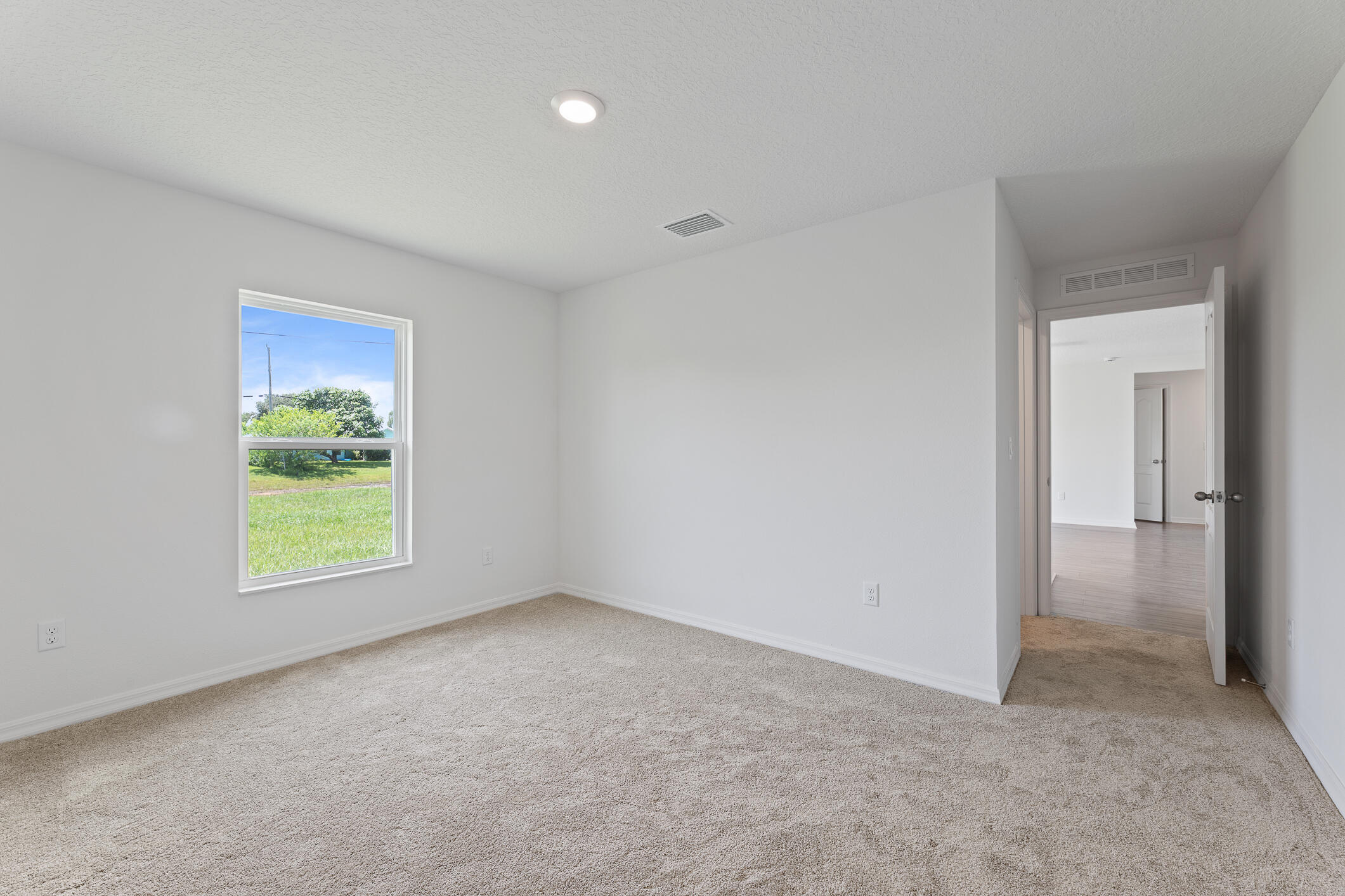 Empty carpeted room with a window overlooking a green lawn and an open doorway.