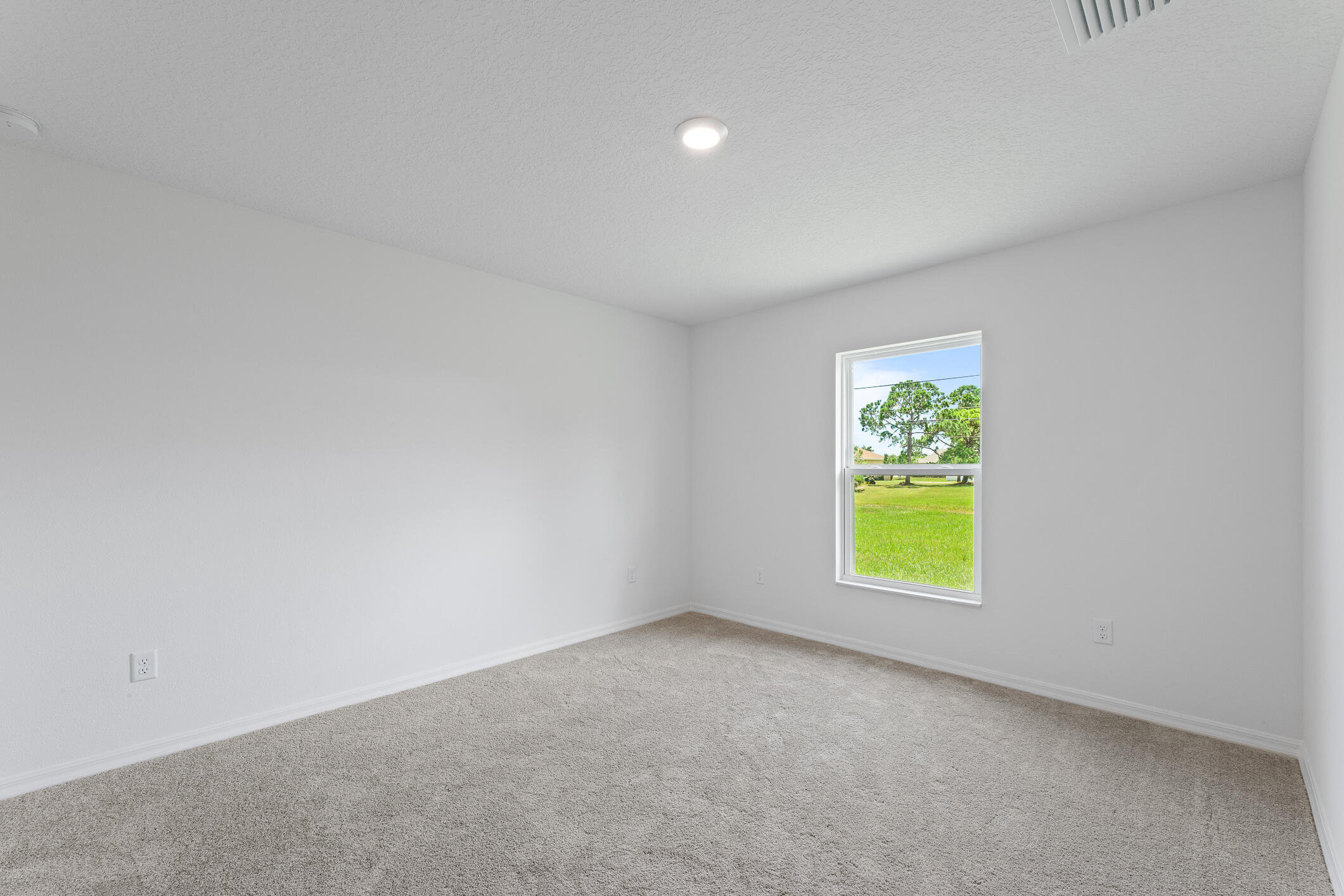 Empty carpeted room with white walls and a window overlooking a green lawn.