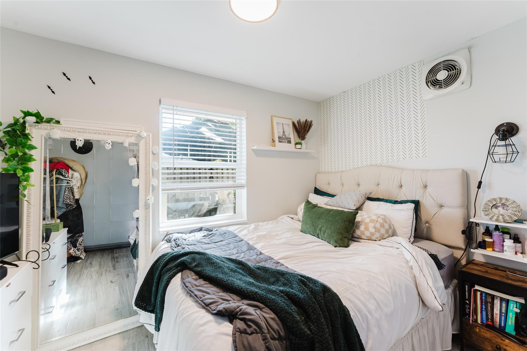 Bedroom with a large bed, patterned accent wall, and full-length mirror beside a window.