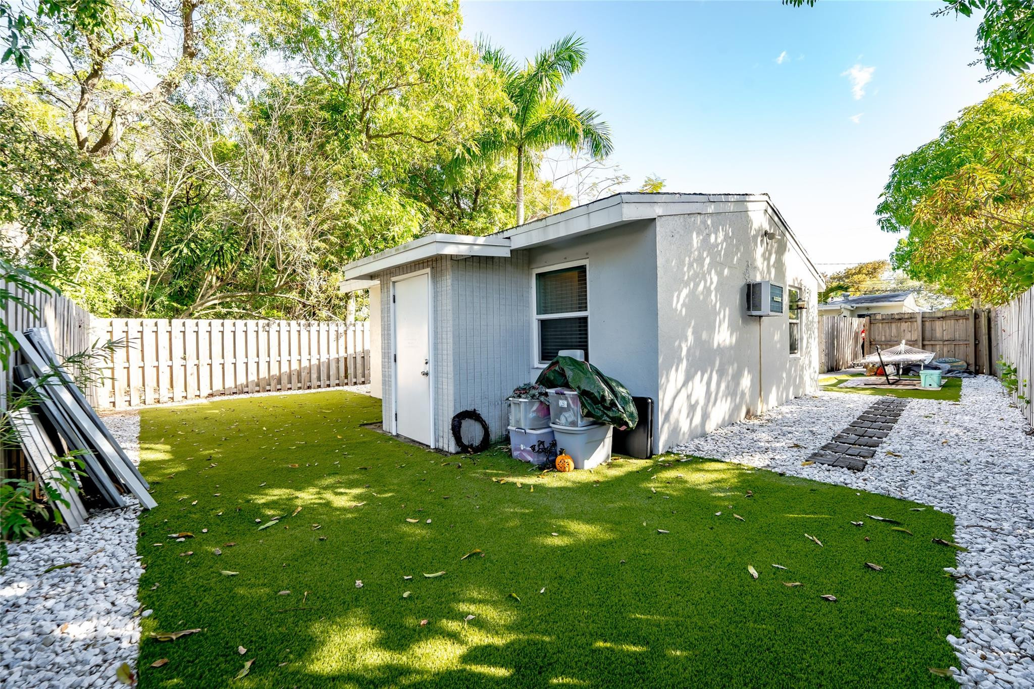 Fenced backyard with green lawn, white gravel paths, and a low flat-roofed structure.