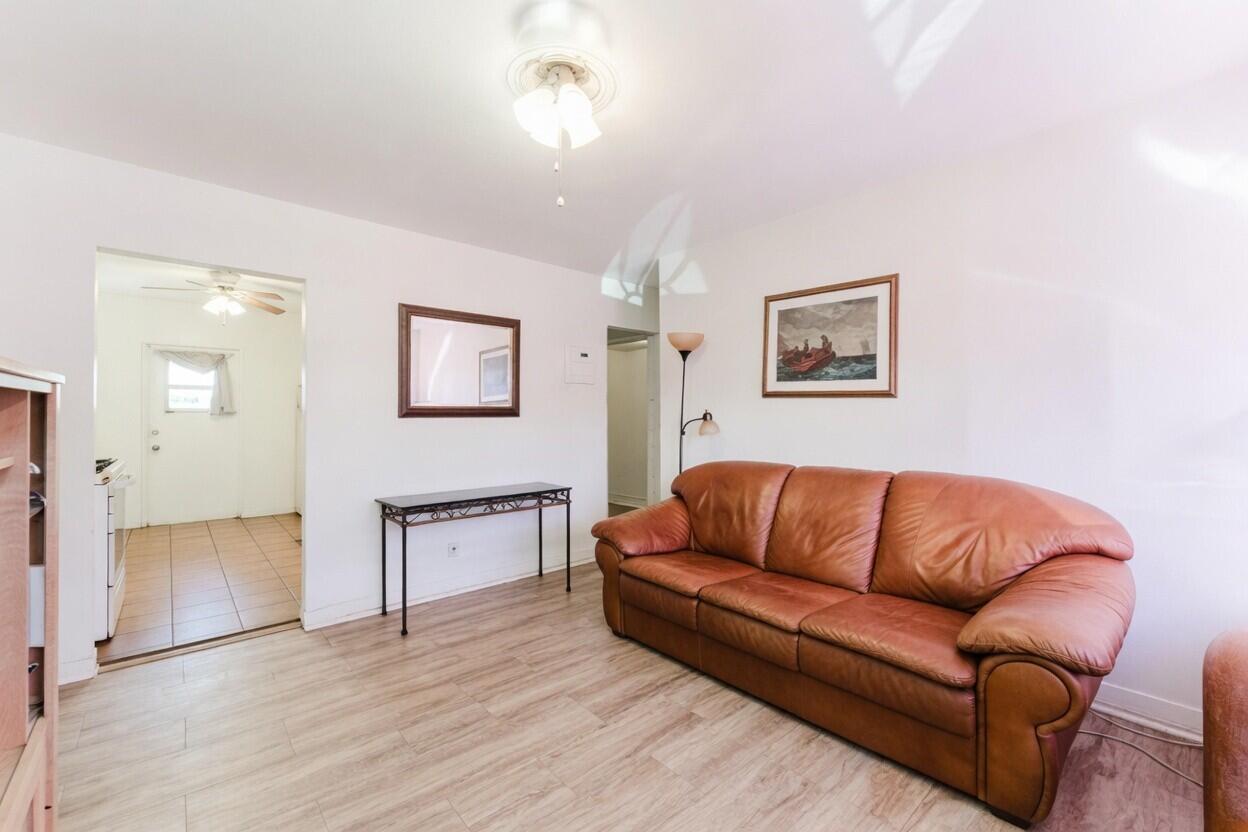 Living room with a brown leather sofa, pale flooring, and an open tiled entryway.