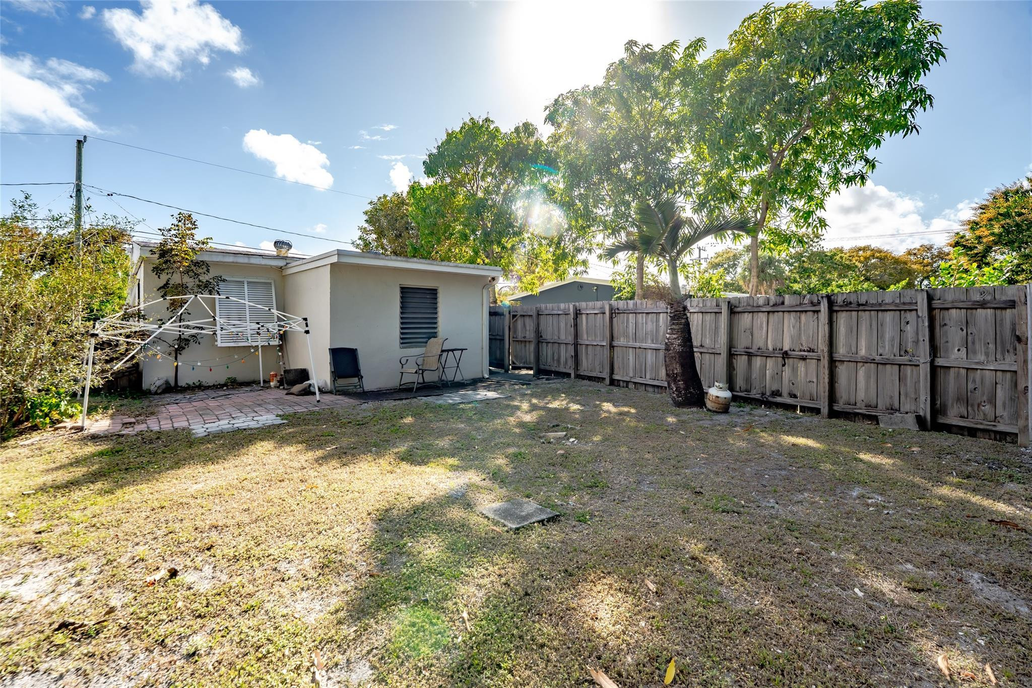 Backyard with a small paved patio, two chairs, mature trees, and a wooden privacy fence.