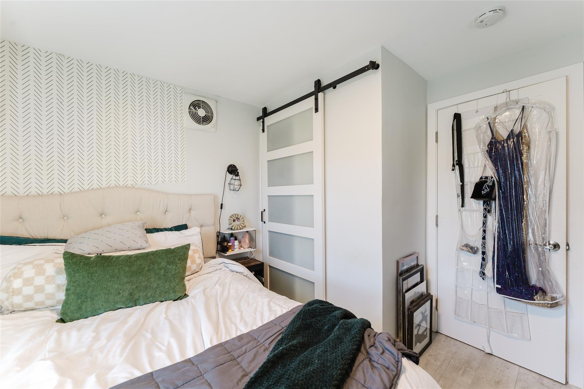 Bedroom with green accent pillows, a patterned wall, and a frosted-glass sliding barn door.