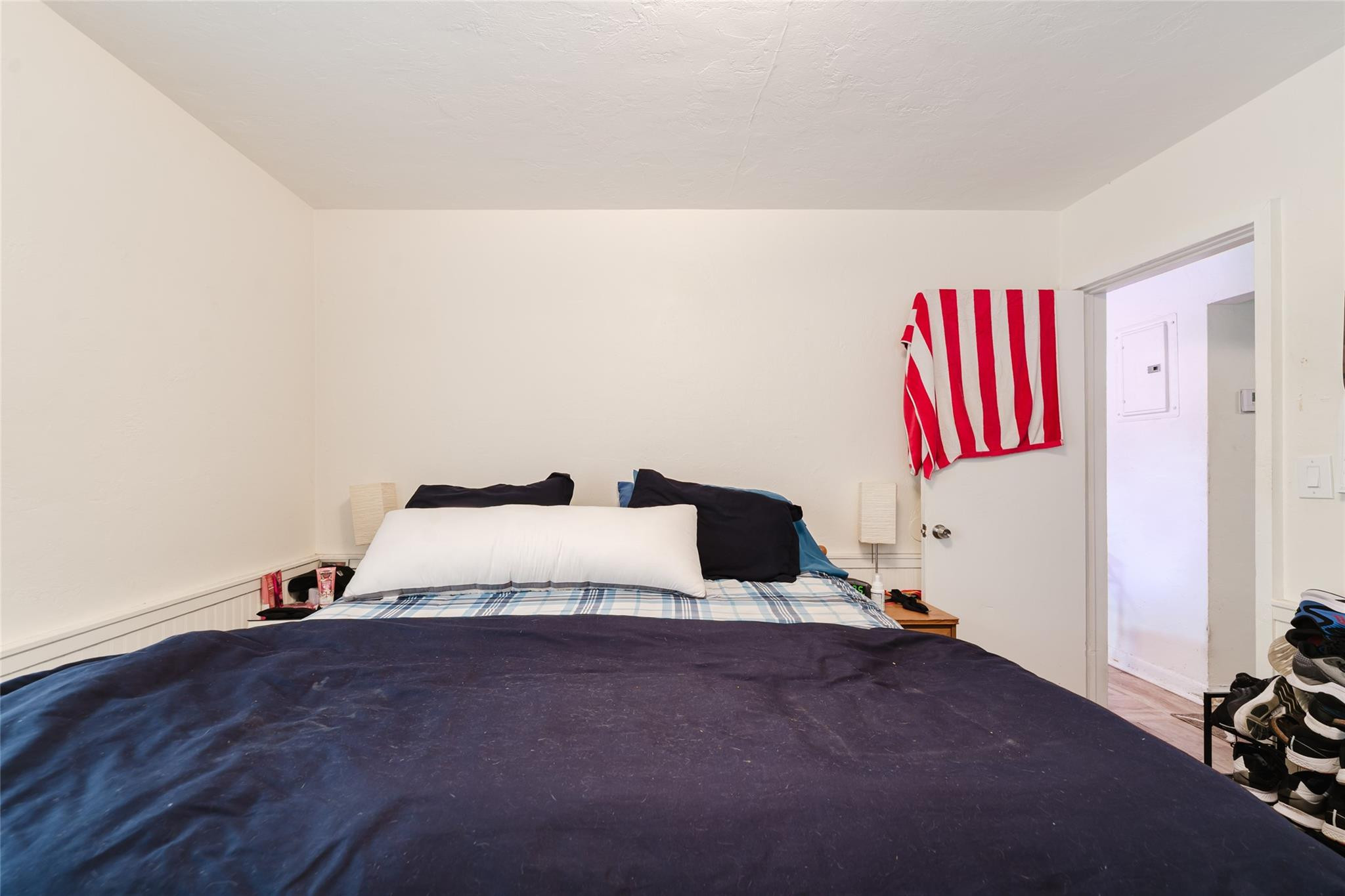 Bedroom with a large navy-covered bed, red-and-white striped towel by the open doorway, and shoes on a rack.
