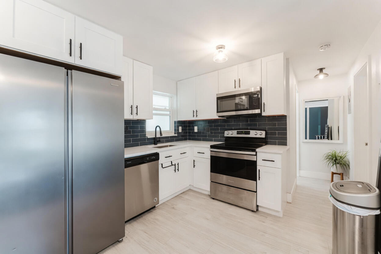 Bright kitchen with white cabinets, stainless steel appliances, and a dark subway-tile backsplash.