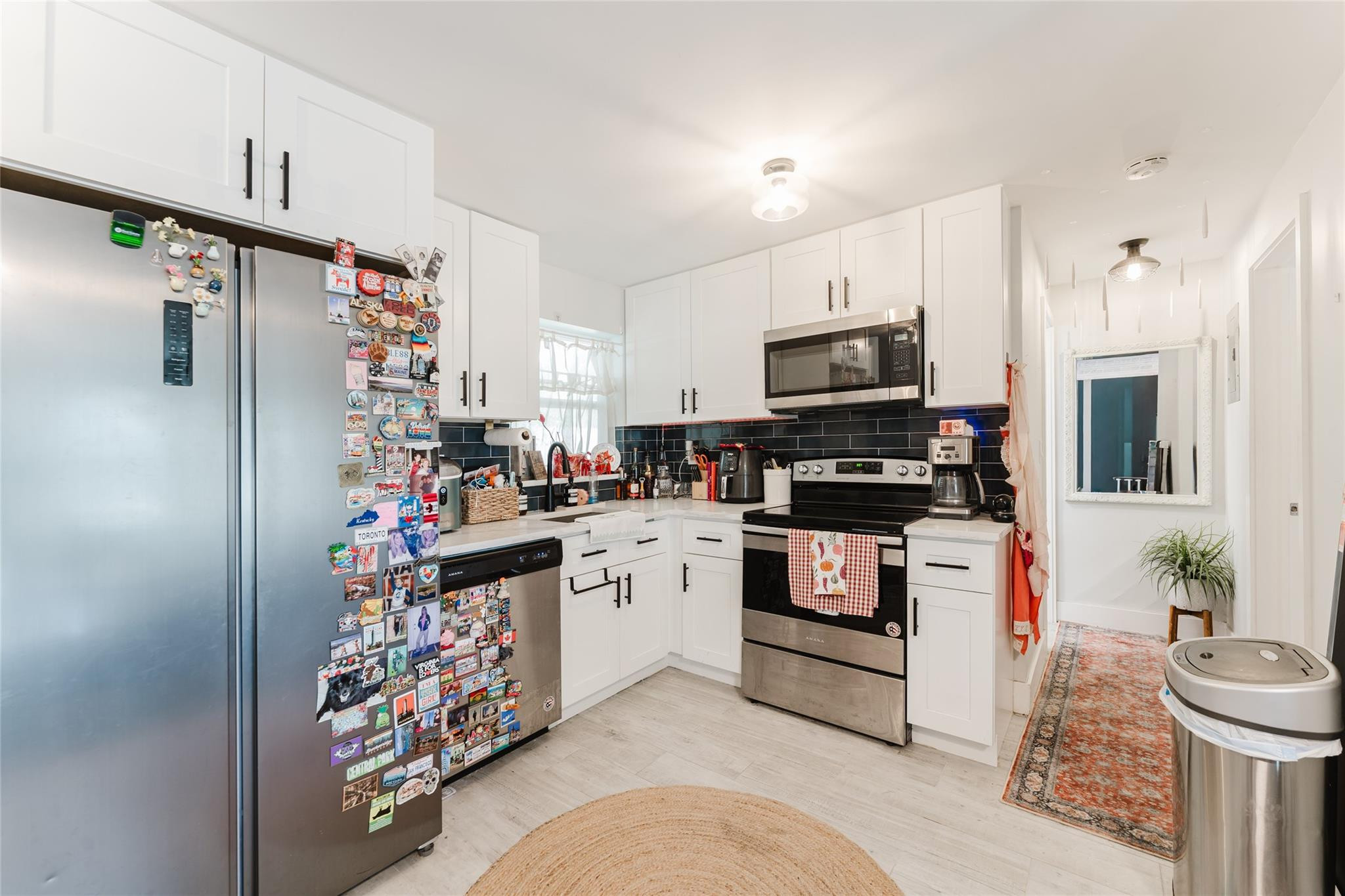 Kitchen with white cabinets, black tile backsplash, and a stainless refrigerator covered in travel magnets.
