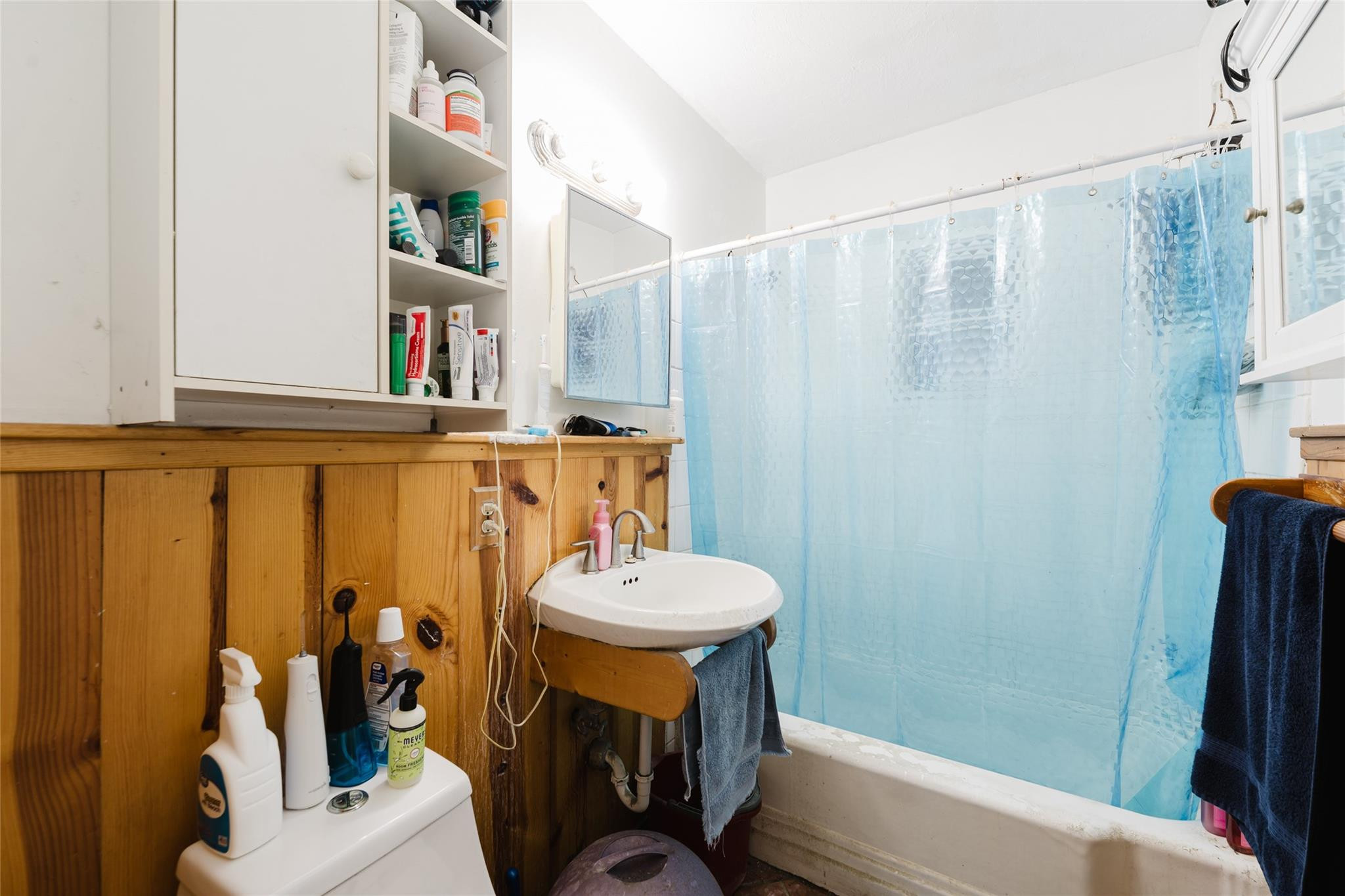 Bathroom with blue shower curtain, small sink, and honey-colored wood paneling.