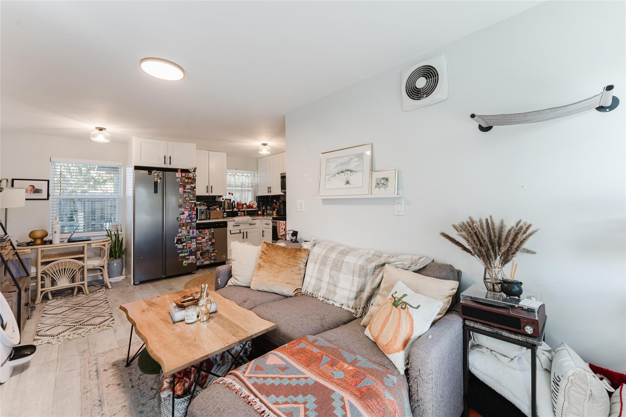 Open-plan living room and kitchen with a gray sectional sofa and magnet-covered stainless steel refrigerator.