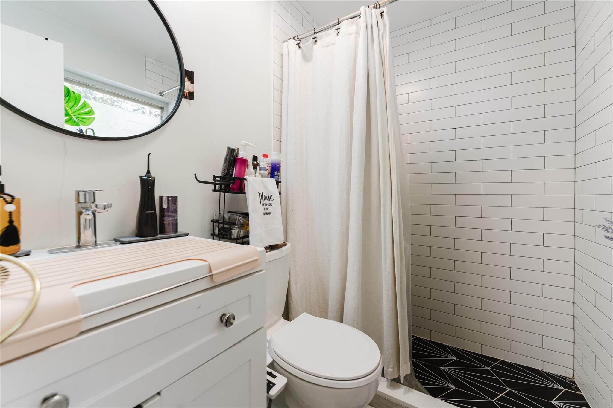 Bathroom with white subway-tile shower, black geometric floor, and white vanity.