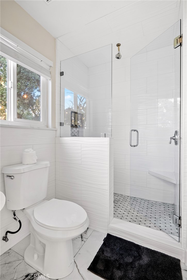 Bathroom with a glass walk-in shower, white tile, and a window beside the toilet.